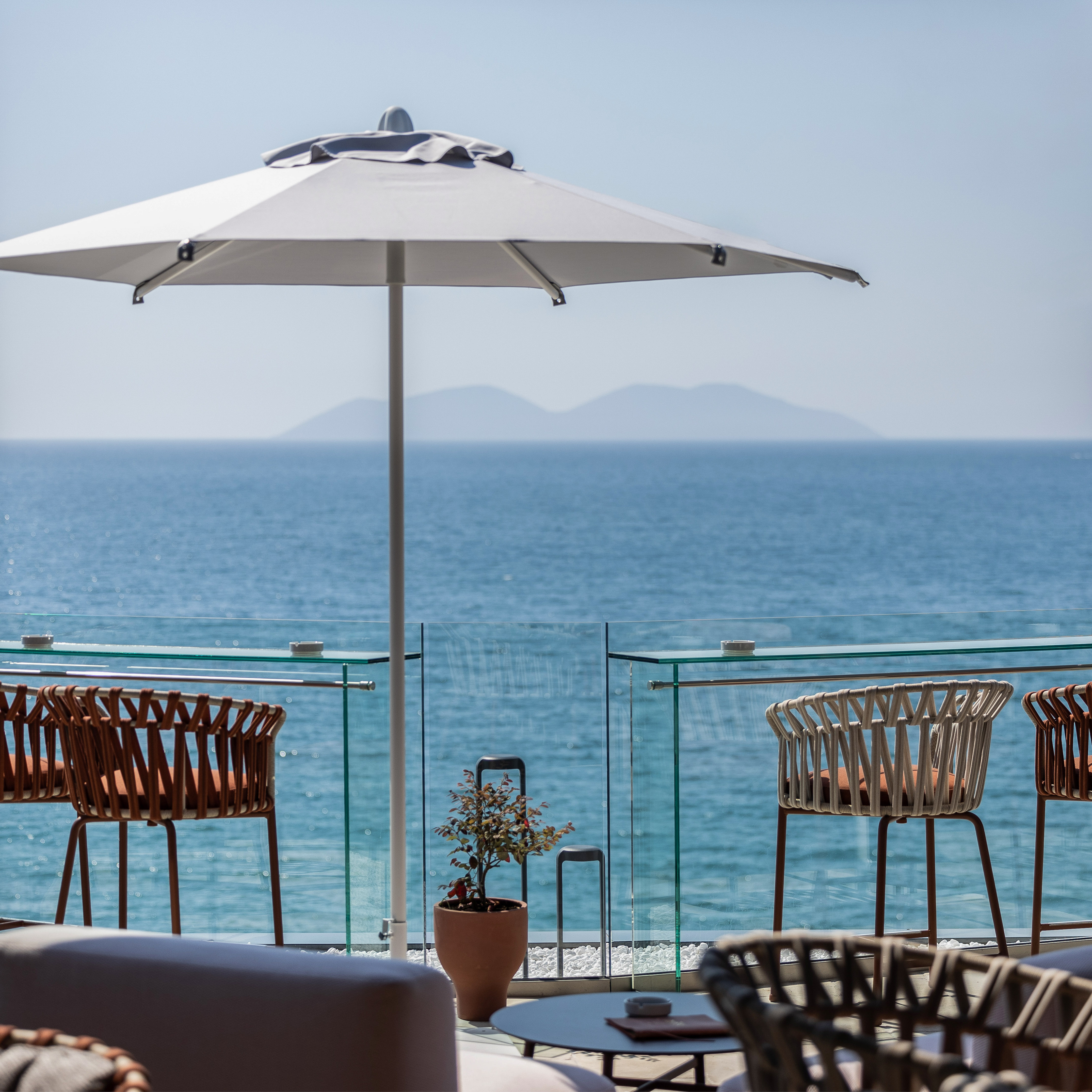 Hotel balcony with ocean view, white umbrella, and modern outdoor chairs.