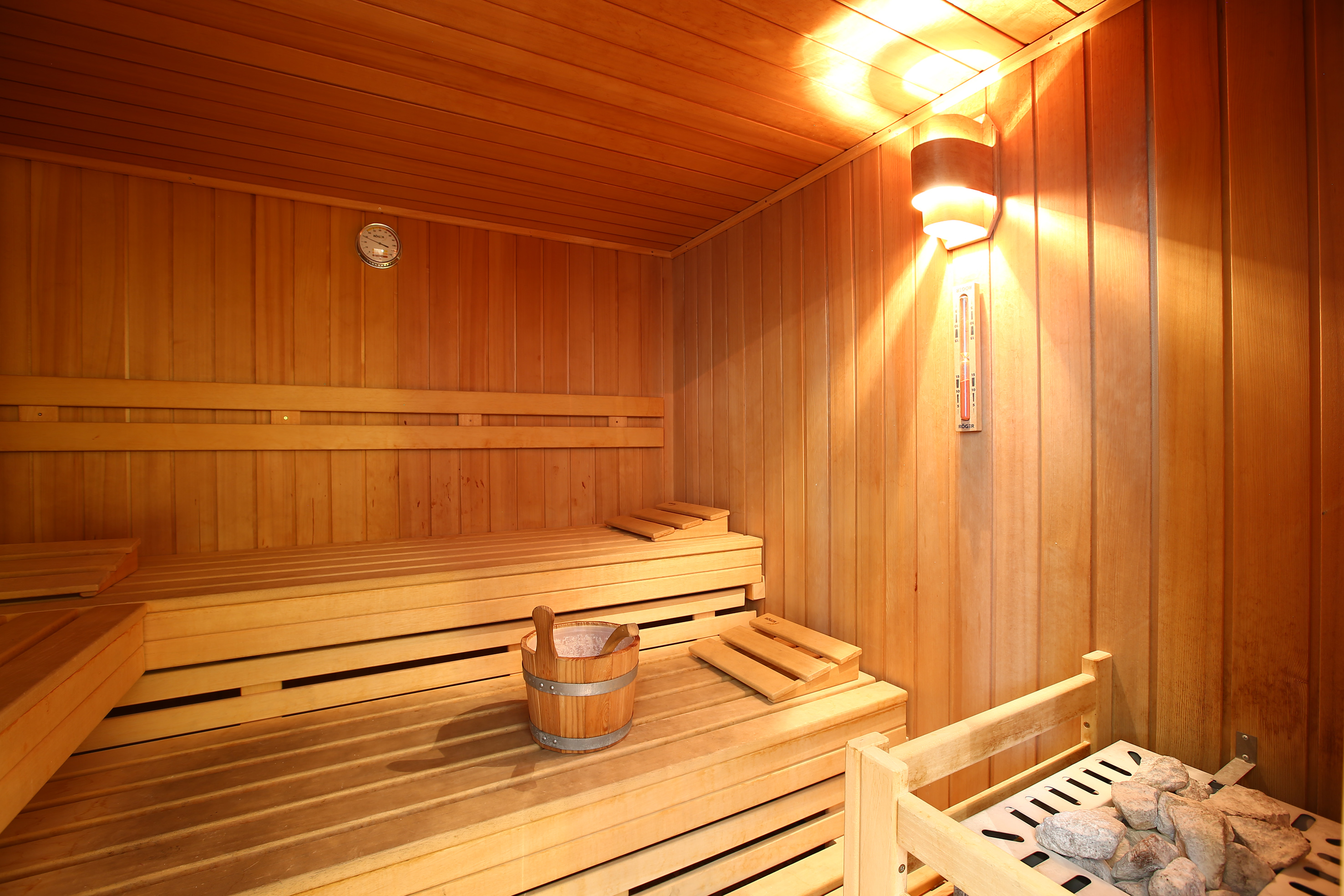 Traditional wooden sauna with benches, bucket, heater, and warm lighting.