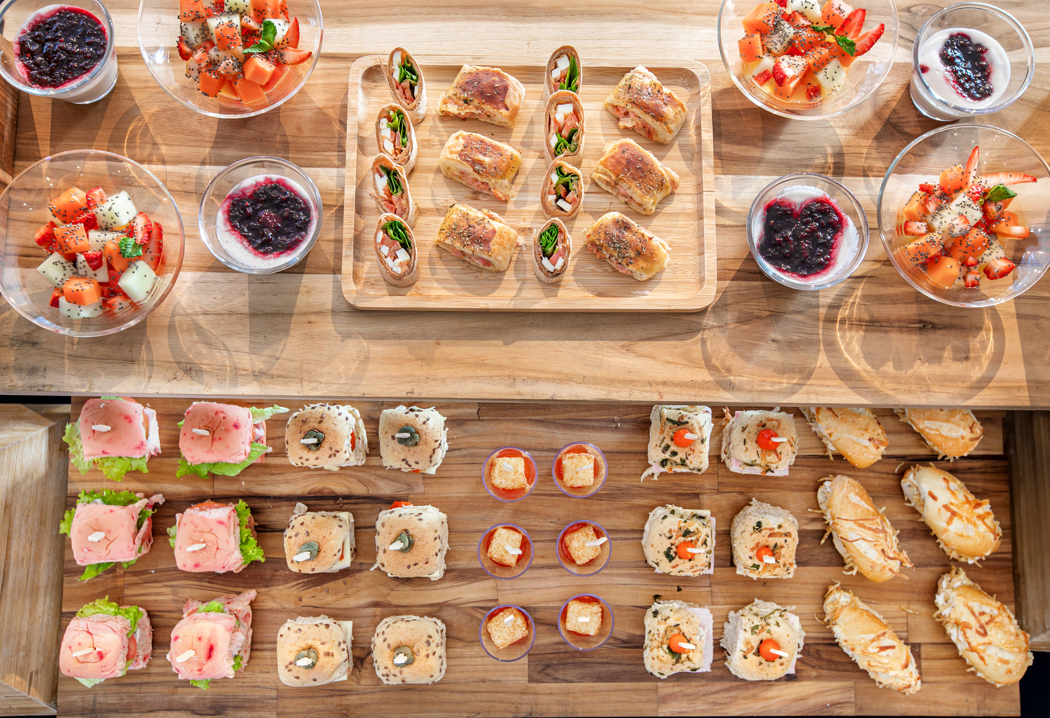 Colorful breakfast/brunch spread: fruit, yogurt, mini sandwiches, and pastries.