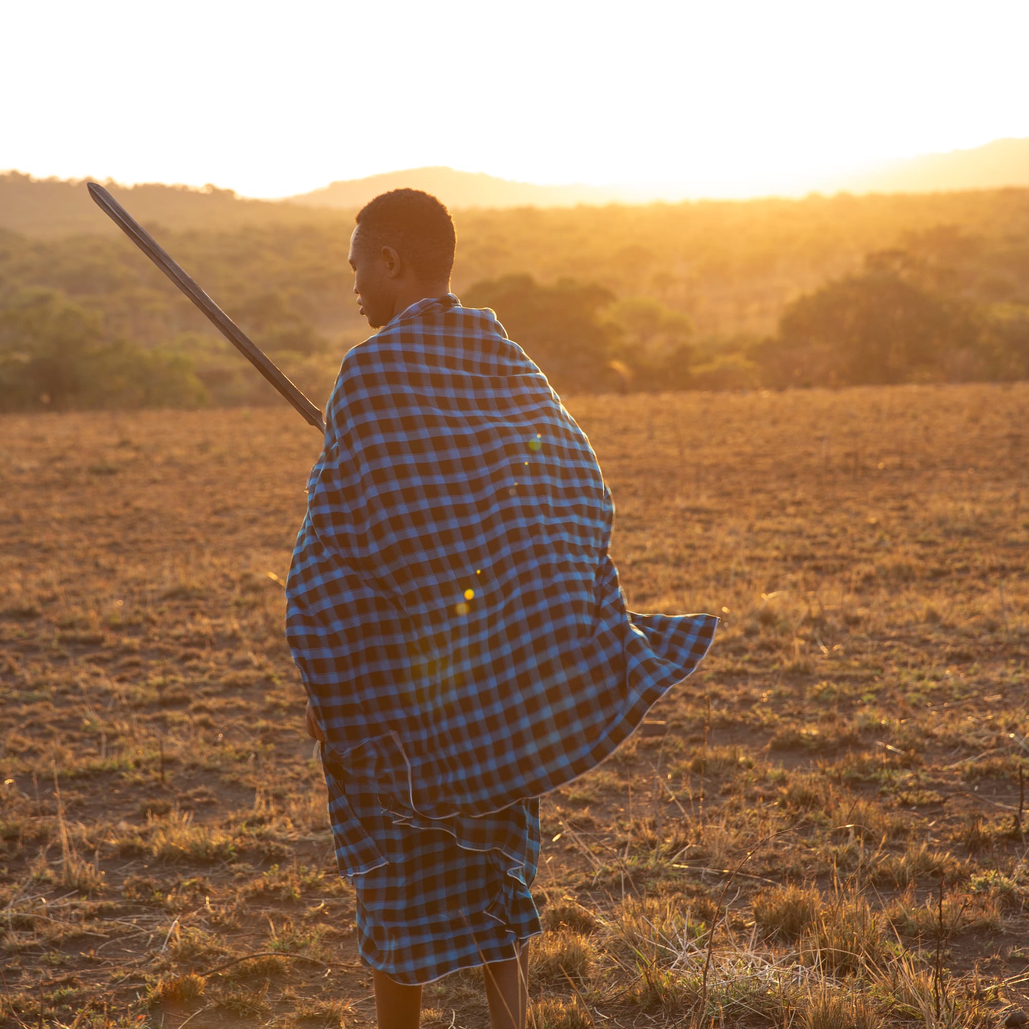 a man in a blue and black plaid robe holding a sword in a field