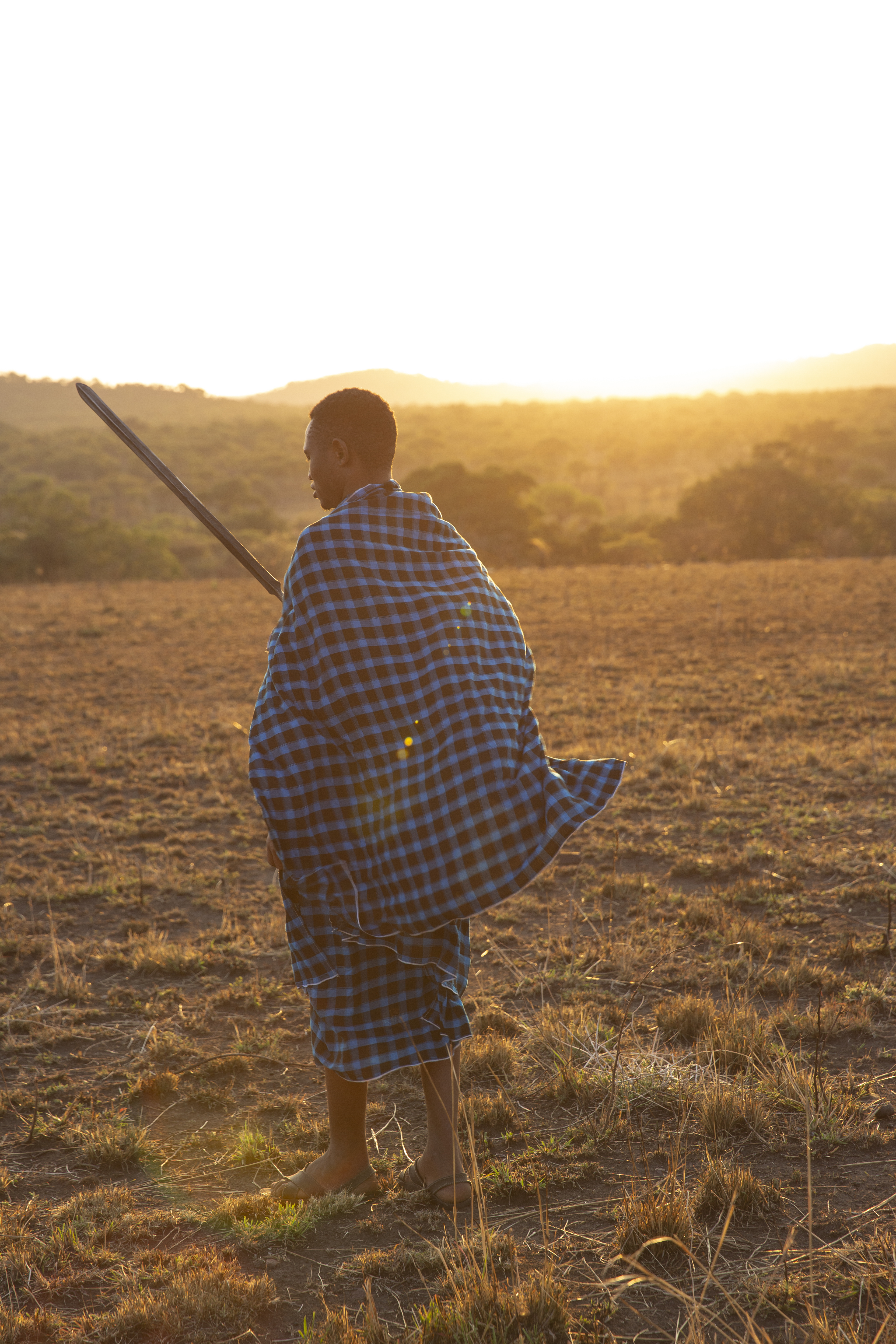a man in a blue and black plaid robe holding a sword in a field