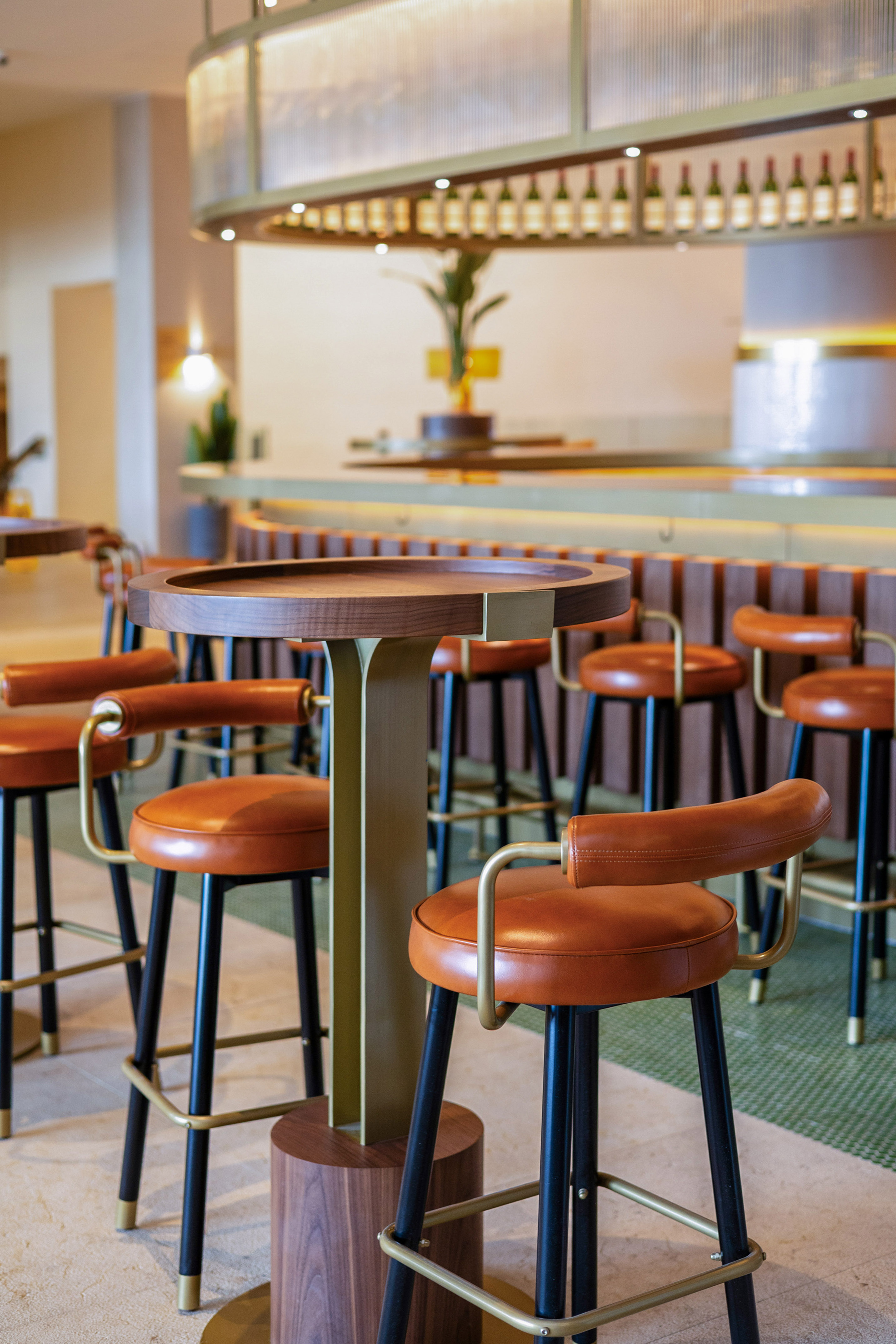 Modern bar interior with brown leather stools, wooden table, and illuminated wine rack.