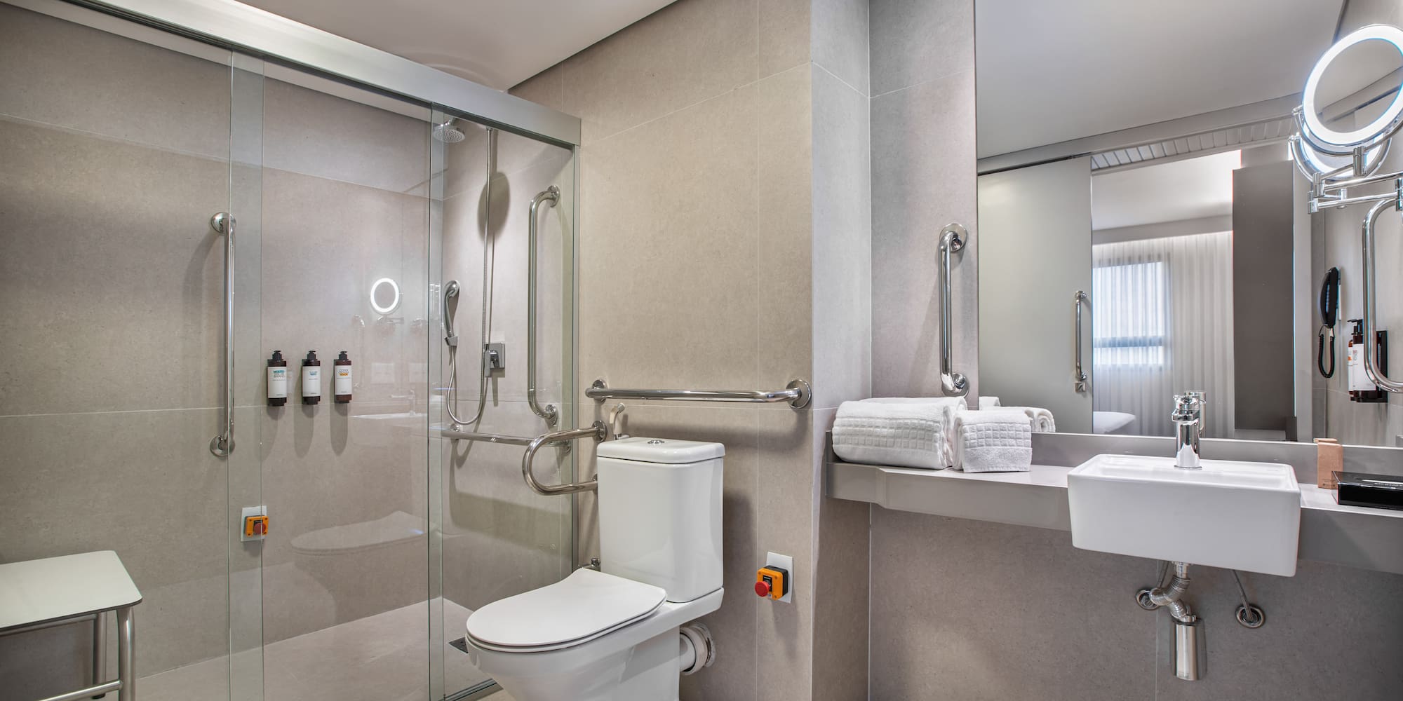 Accessible hotel bathroom: roll-in shower, grab bars, toilet, emergency button.