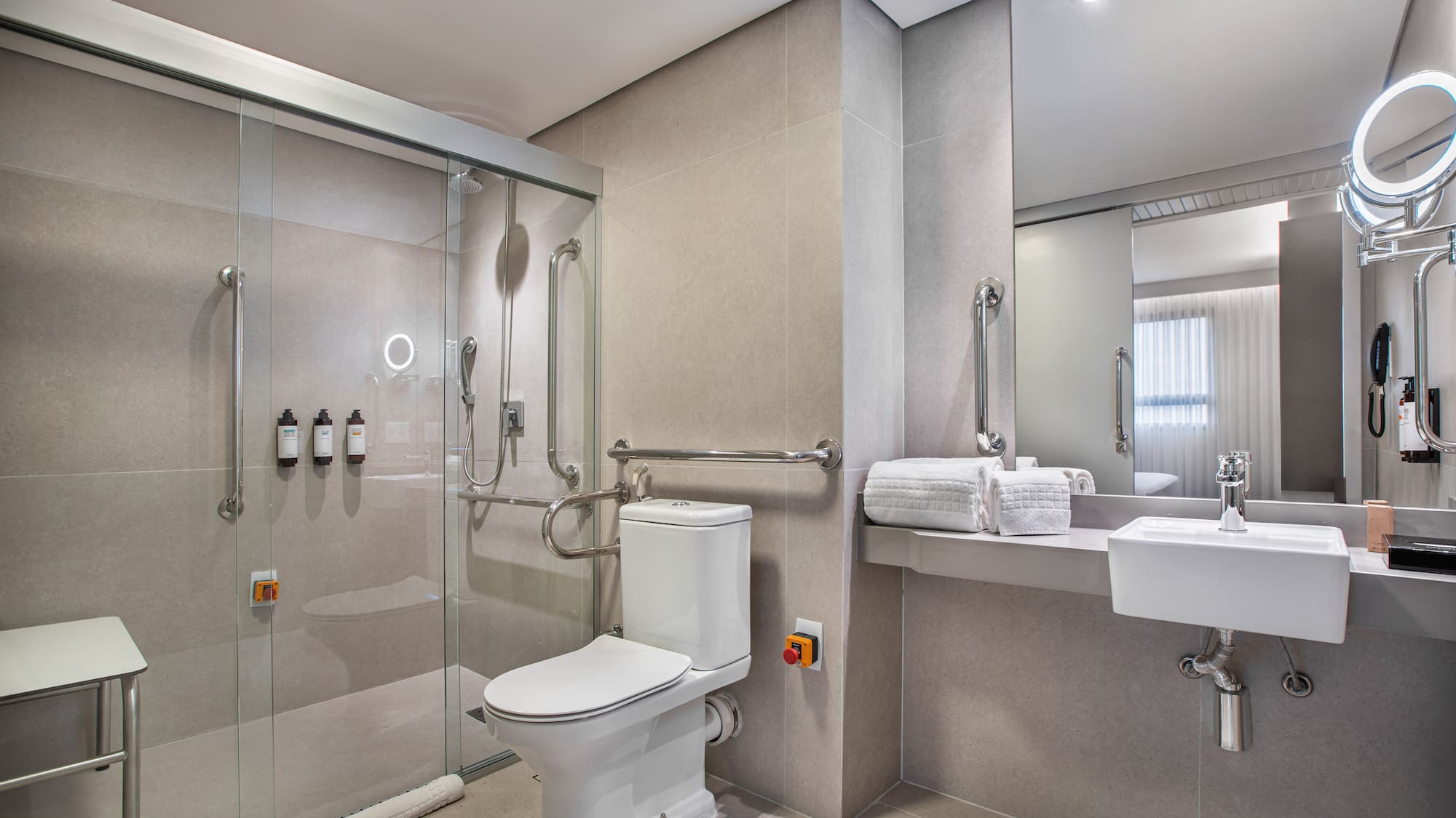 Accessible hotel bathroom: roll-in shower, grab bars, toilet, emergency button.