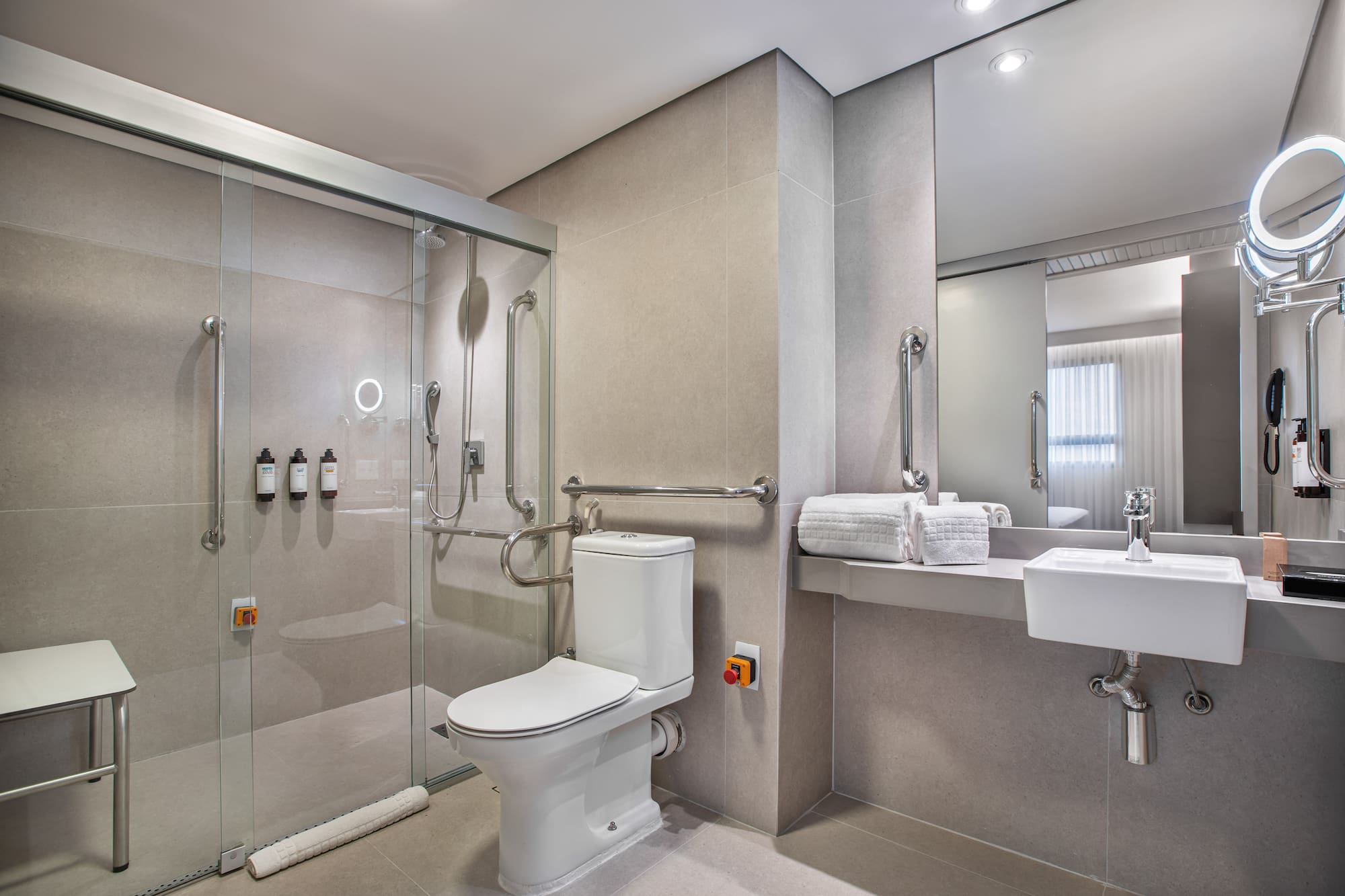Accessible hotel bathroom: roll-in shower, grab bars, toilet, emergency button.