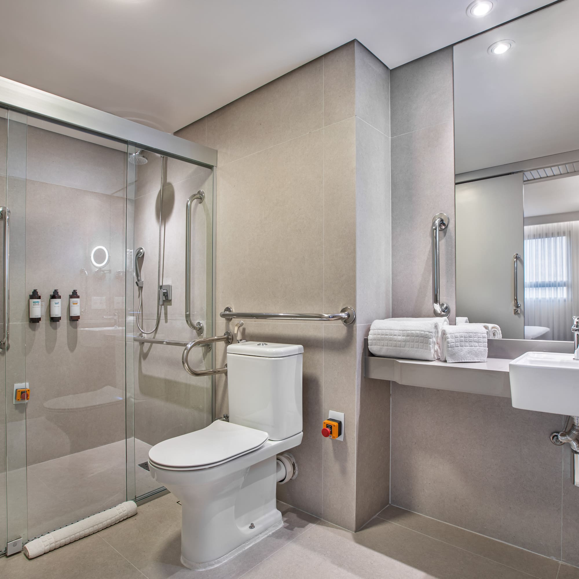 Accessible hotel bathroom: roll-in shower, grab bars, toilet, emergency button.