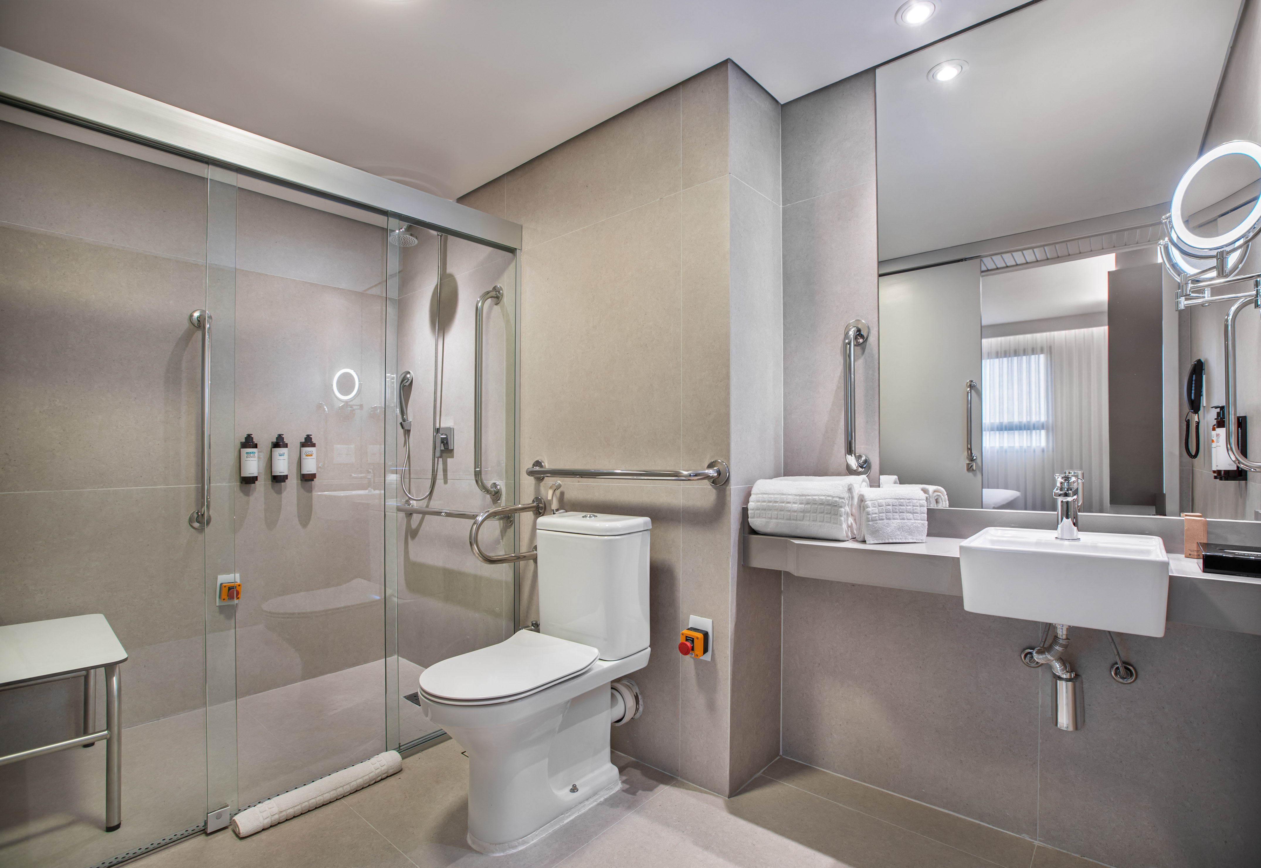 Accessible hotel bathroom: roll-in shower, grab bars, toilet, emergency button.