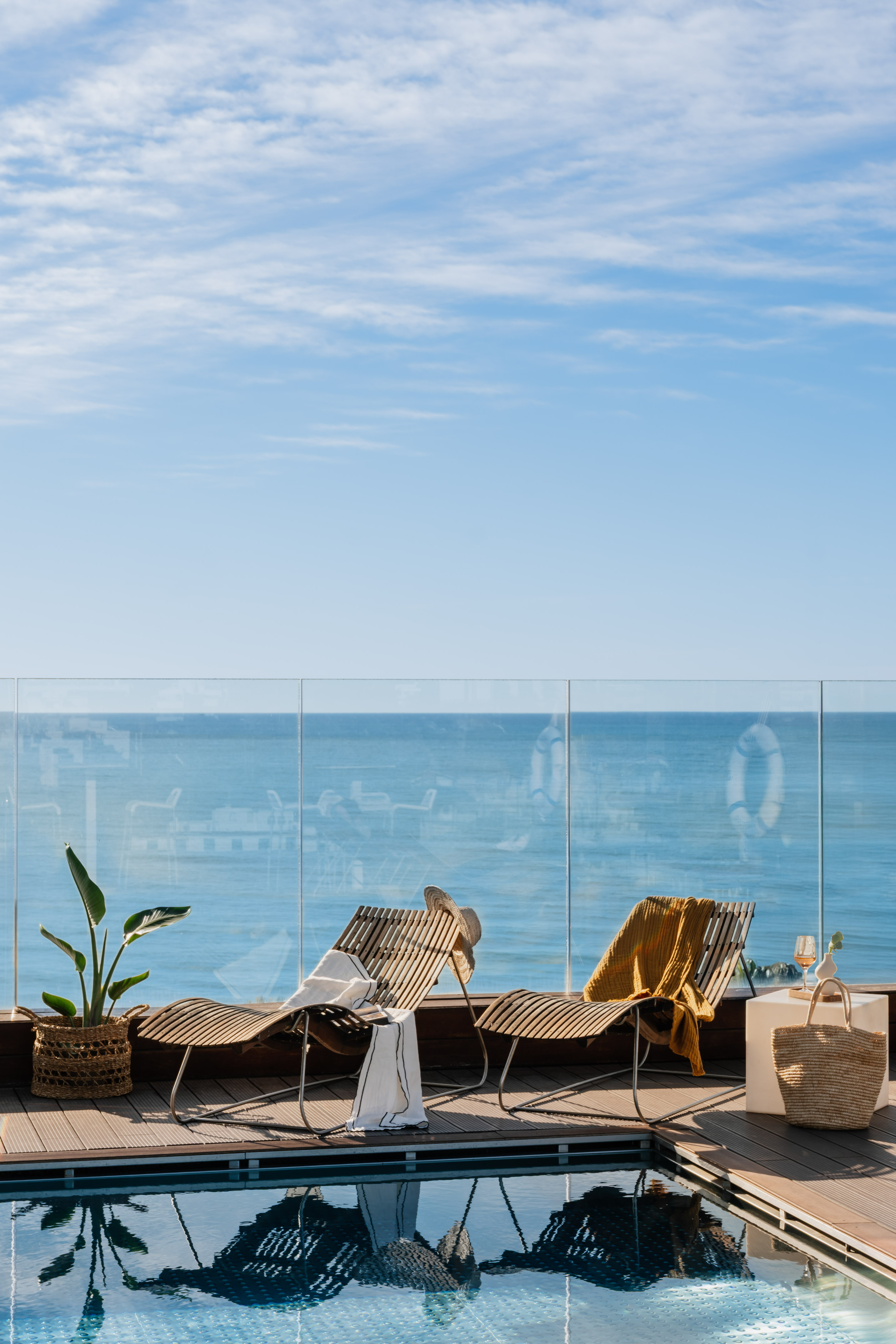 Luxury resort infinity pool deck with wooden lounge chairs and ocean view.