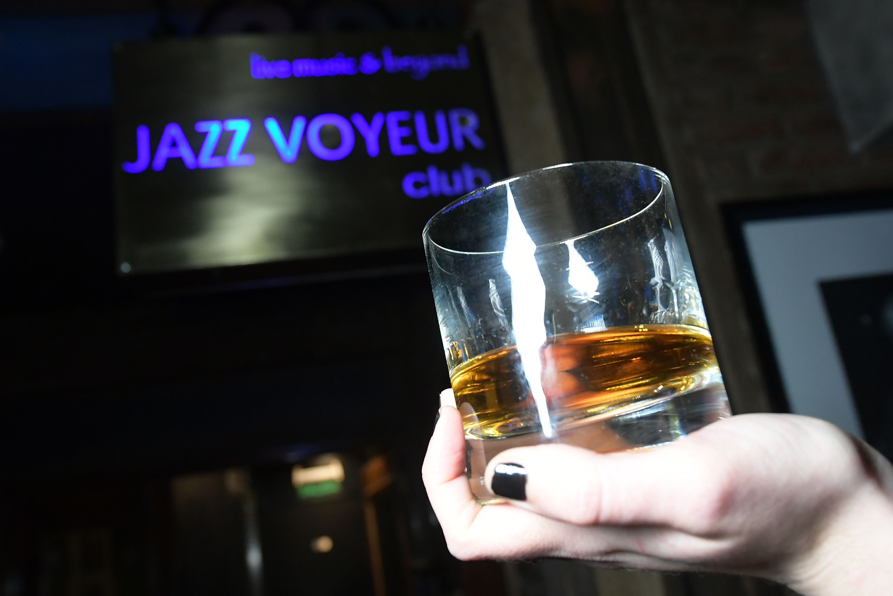 Whiskey glass held at Jazz Voyeur Club, glowing live music sign in background. - Jazz Voyeur Club - Melia Recoleta Plaza, Buenos Aires