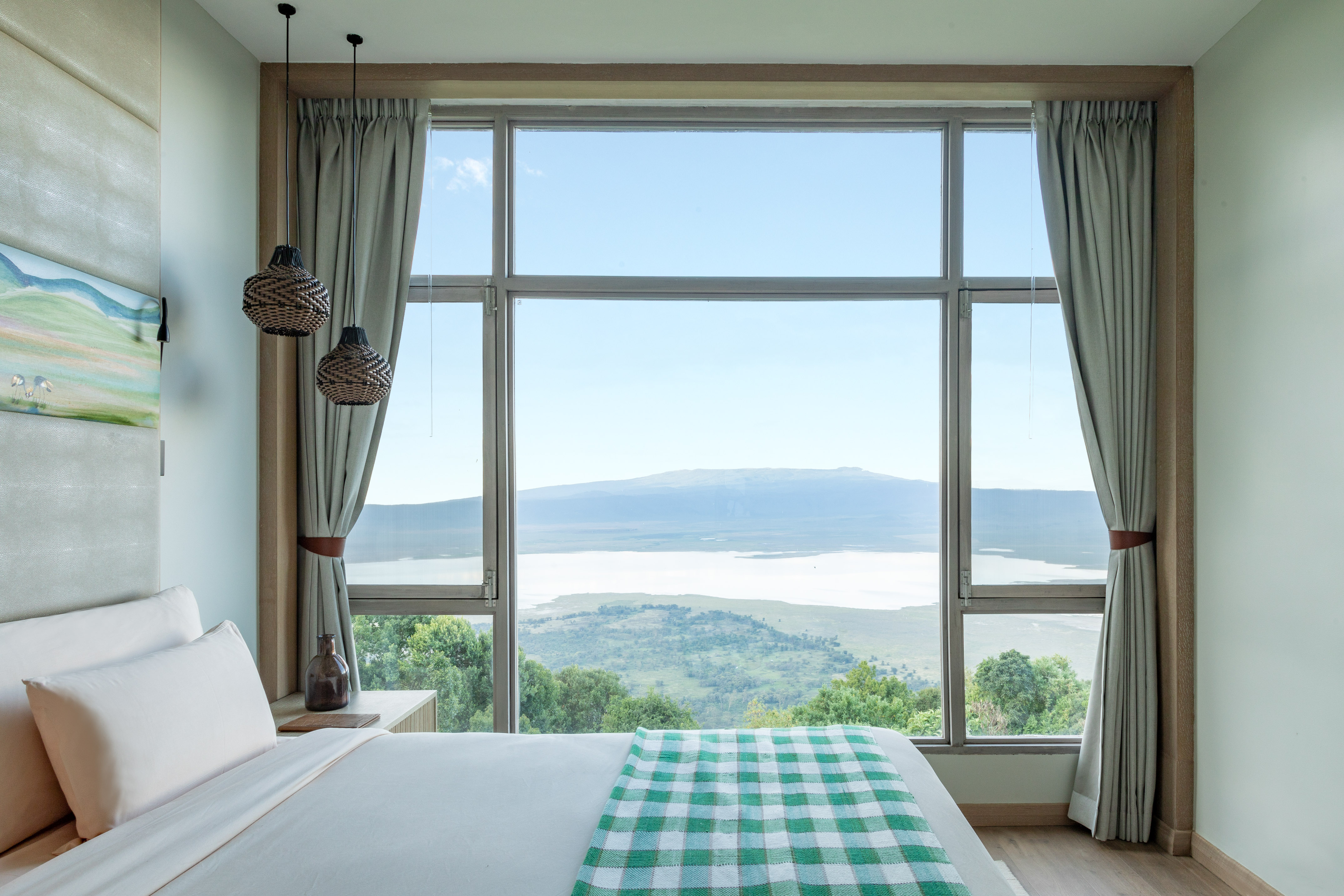 Modern bedroom with lake and mountain view. White bed, green checkered throw.