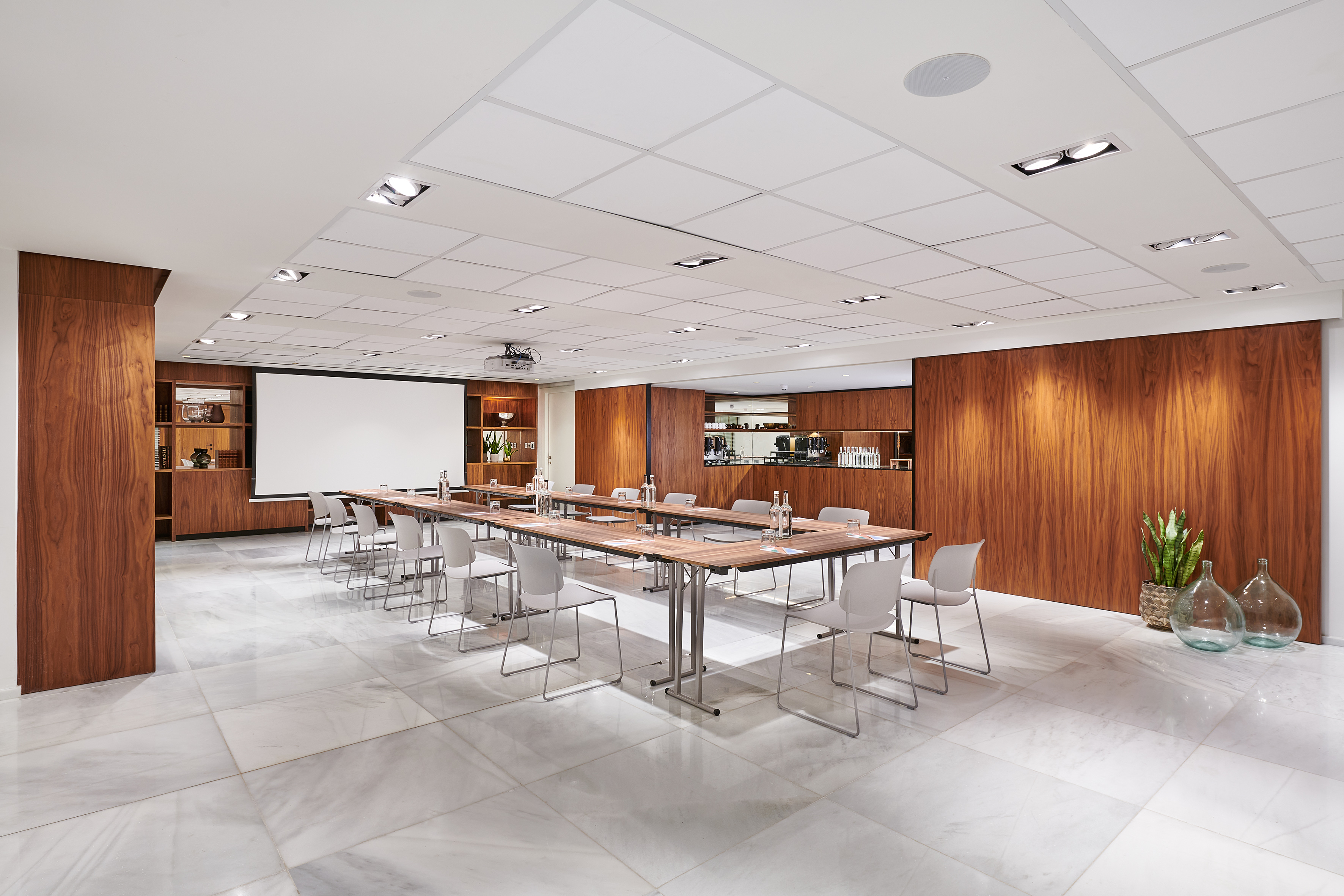 Modern conference room with U-shaped table, projector, marble floor, and wood paneling.
