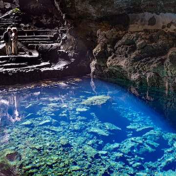people standing on stairs in a cave with clear blue water