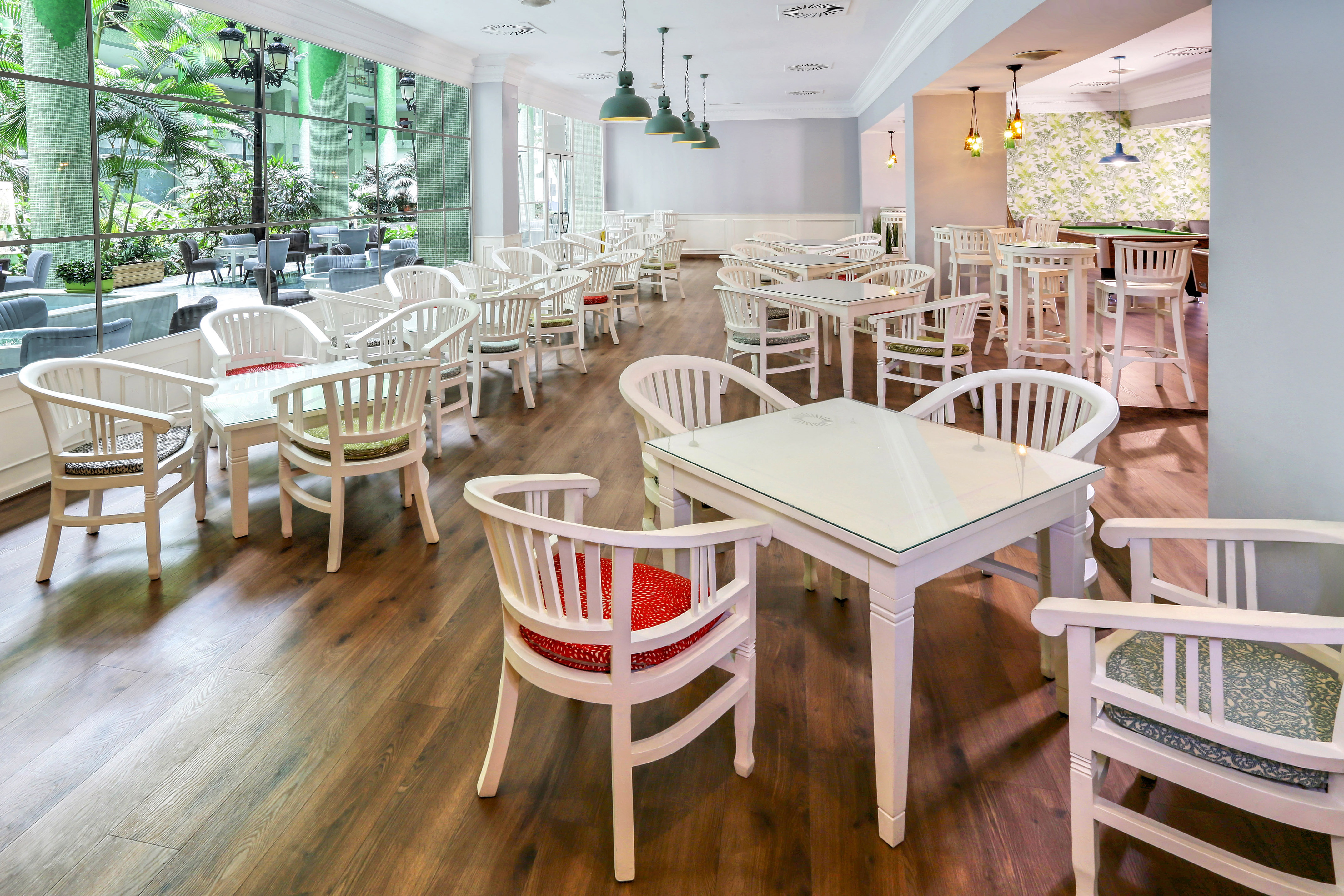 White furniture in a hotel cafe lounge with garden view and billiards table.