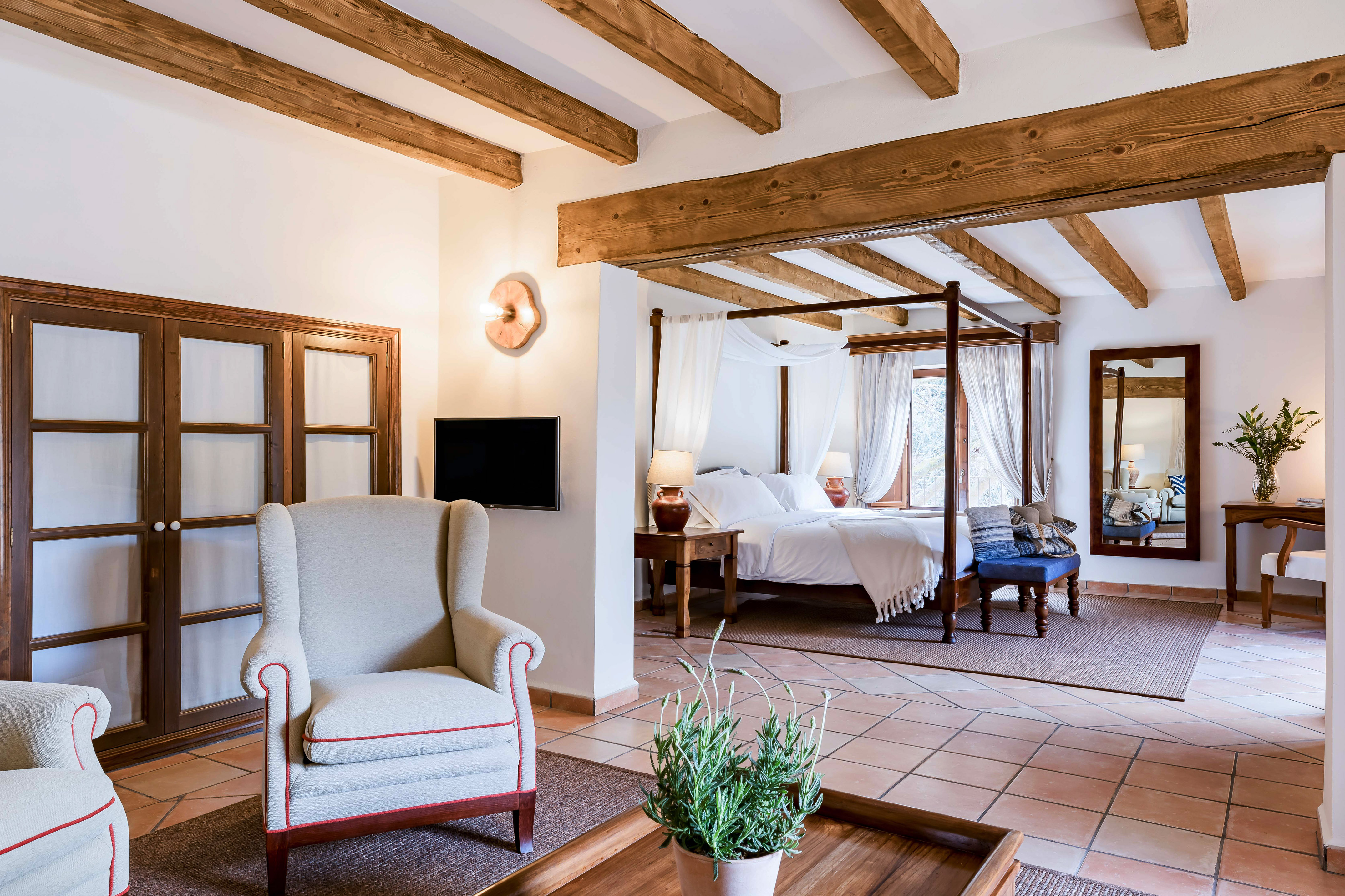 Rustic hotel suite with four-poster bed, exposed wooden beams, and living area.