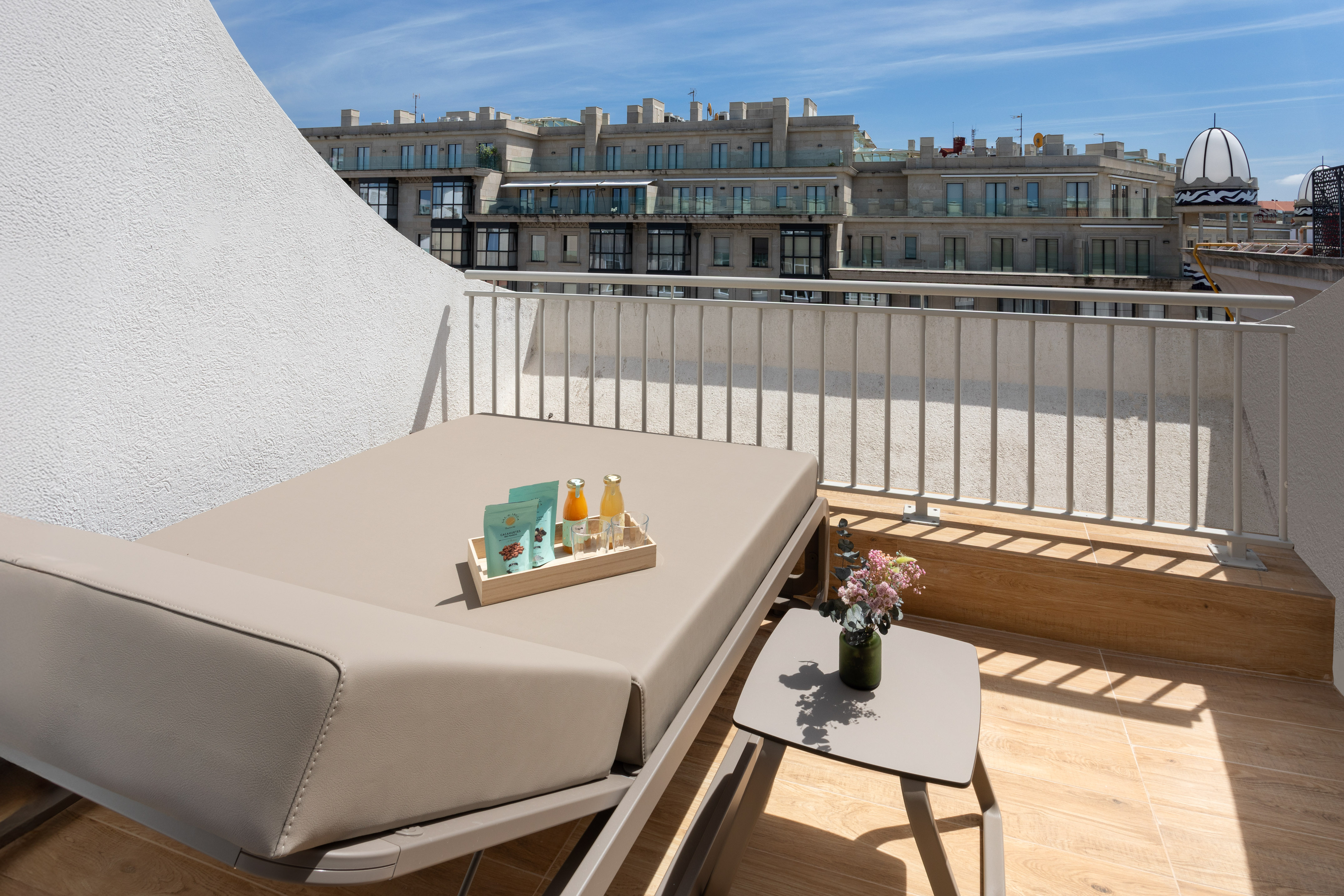 Modern hotel balcony with lounge daybed, refreshments, and city skyline view.
