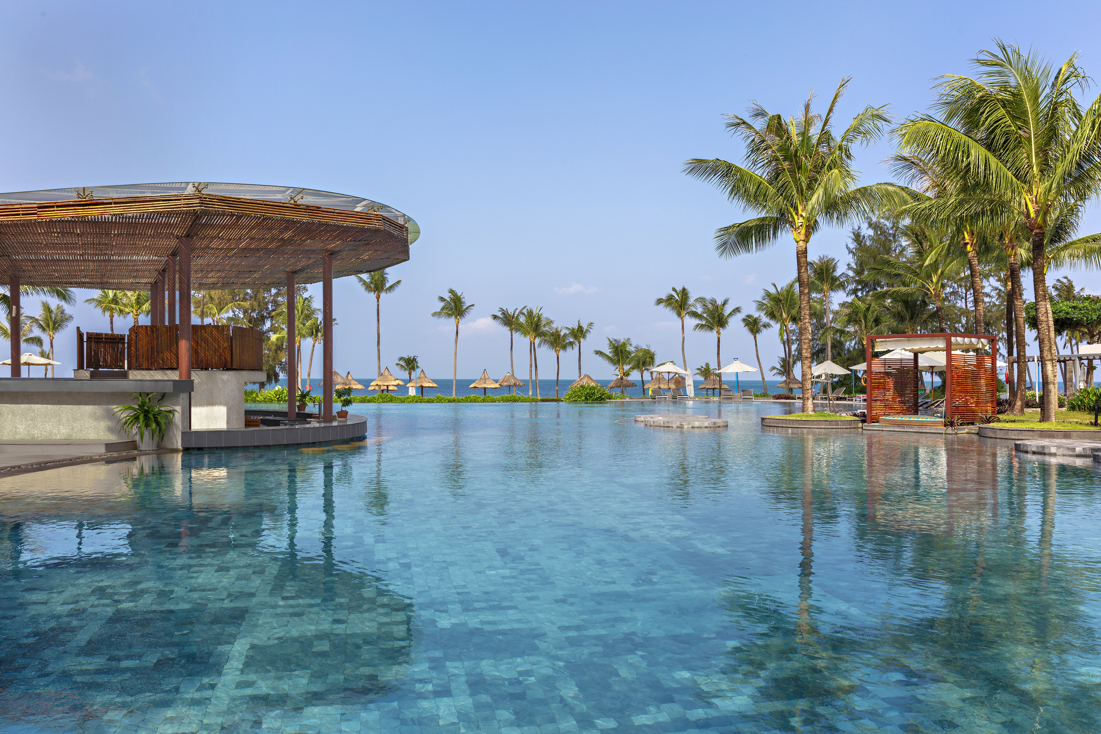 Luxury resort swimming pool with tropical bar, palm trees, and ocean view.