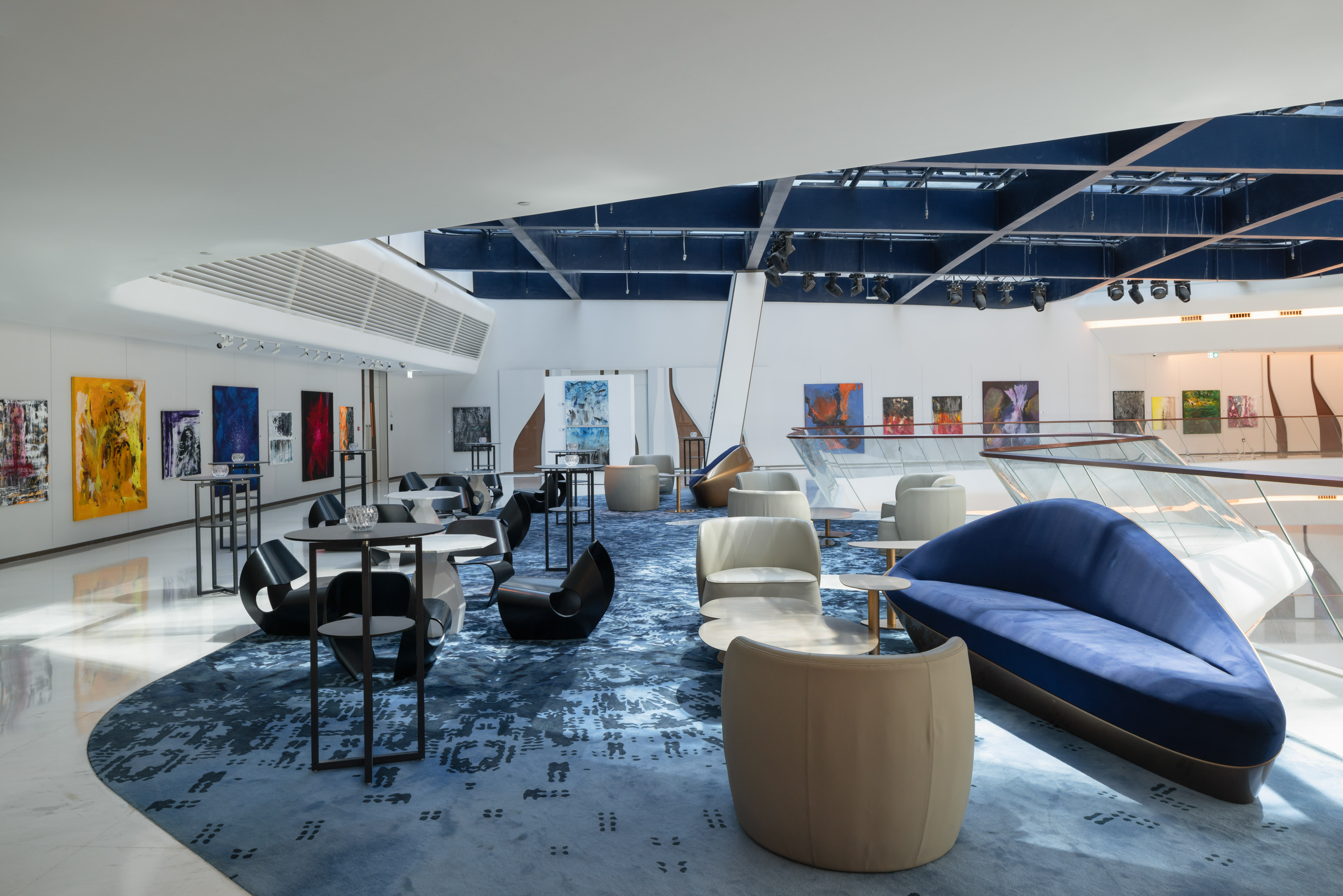 Modern lounge with blue patterned carpet, contemporary seating, and abstract art gallery walls.
