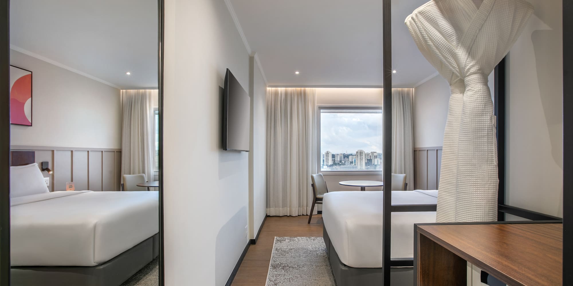 Modern hotel room with king bed, city view, bathrobe, and in-room safe.
