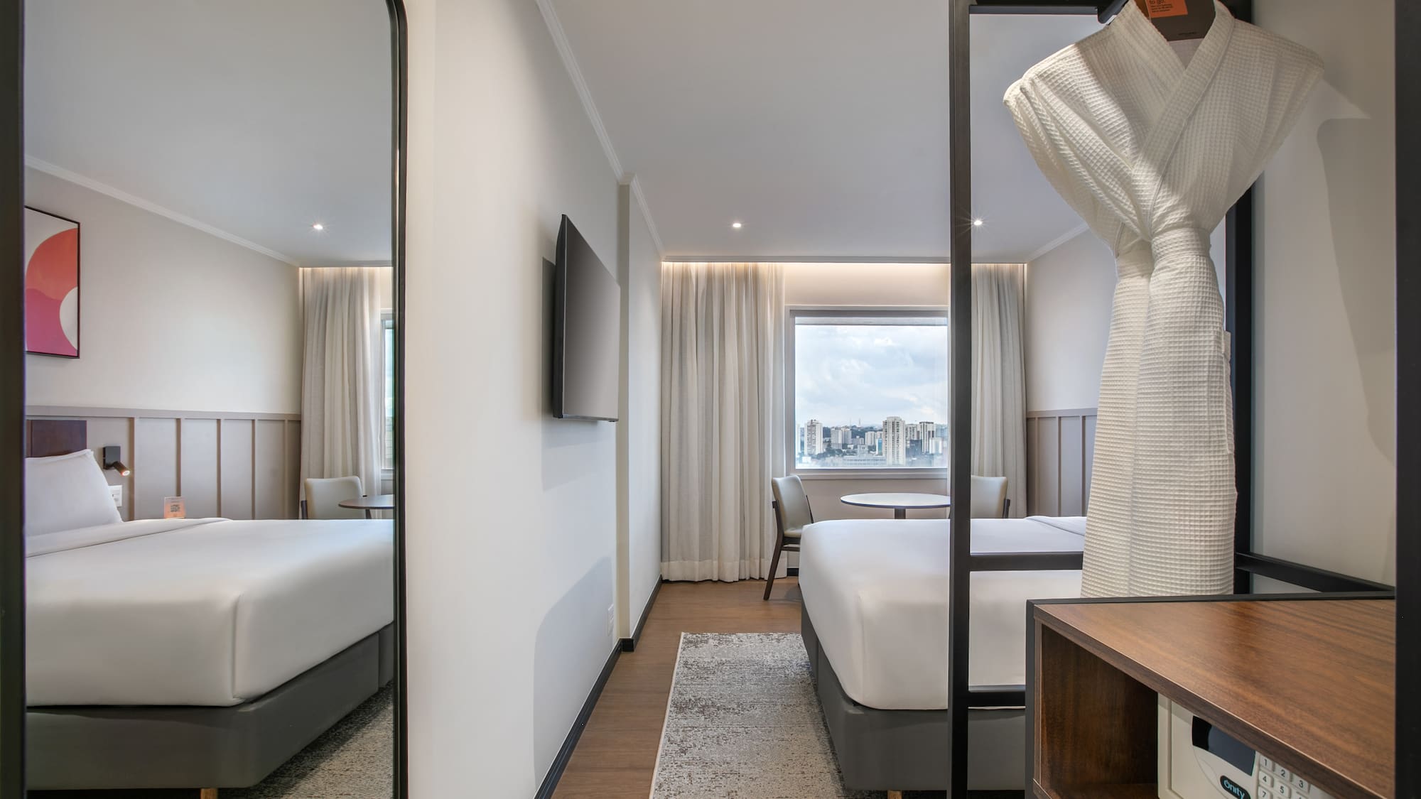 Modern hotel room with king bed, city view, bathrobe, and in-room safe.