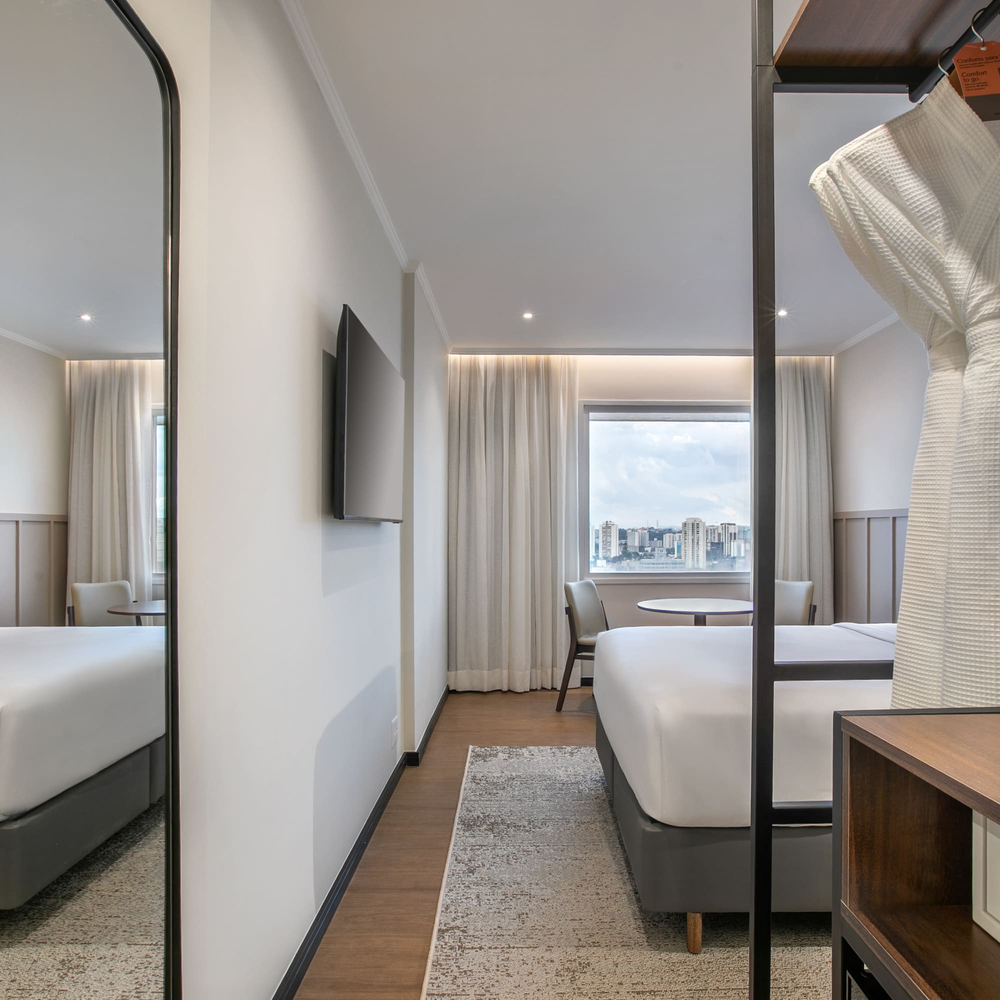 Modern hotel room with king bed, city view, bathrobe, and in-room safe.