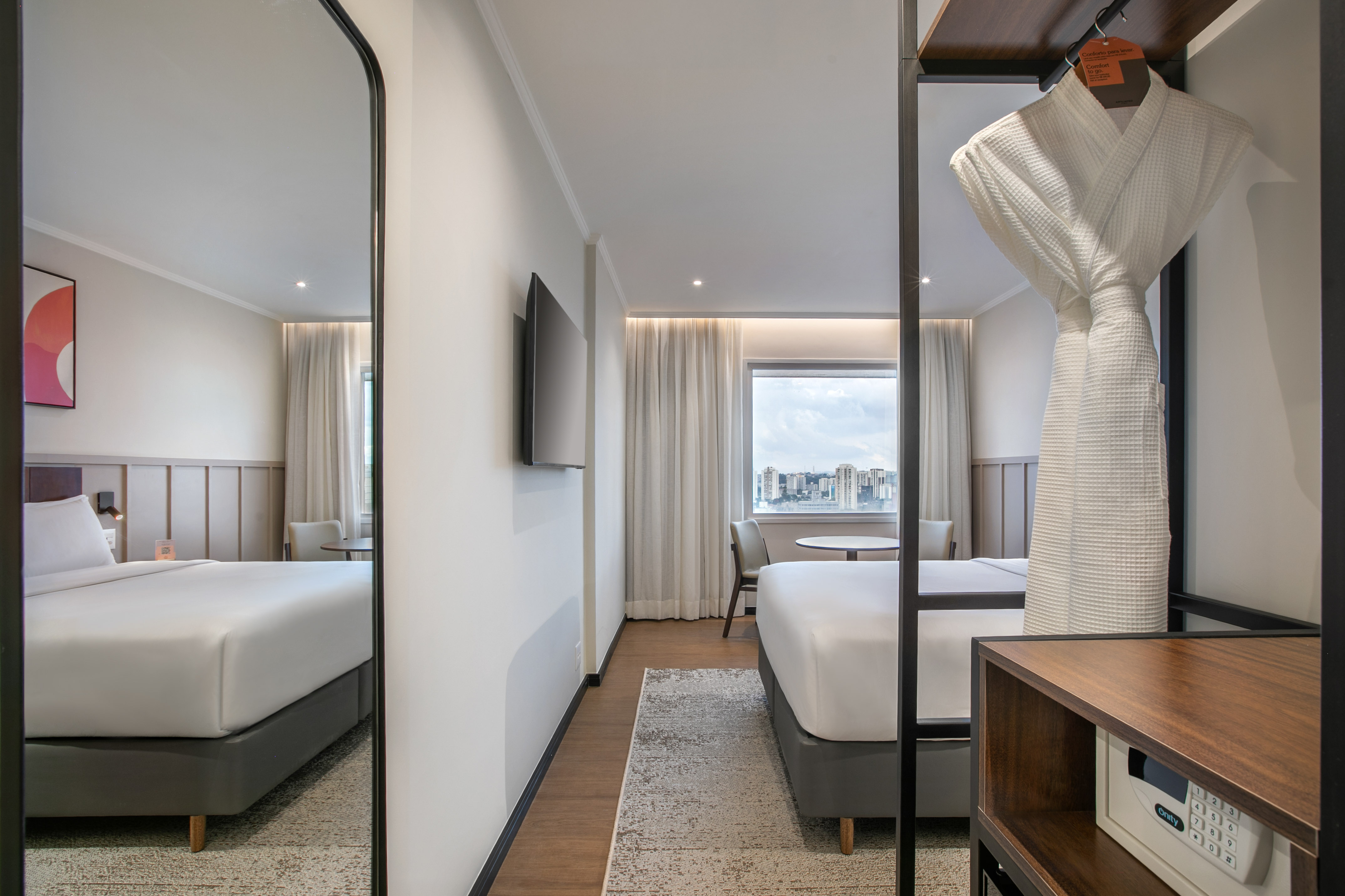 Modern hotel room with king bed, city view, bathrobe, and in-room safe.