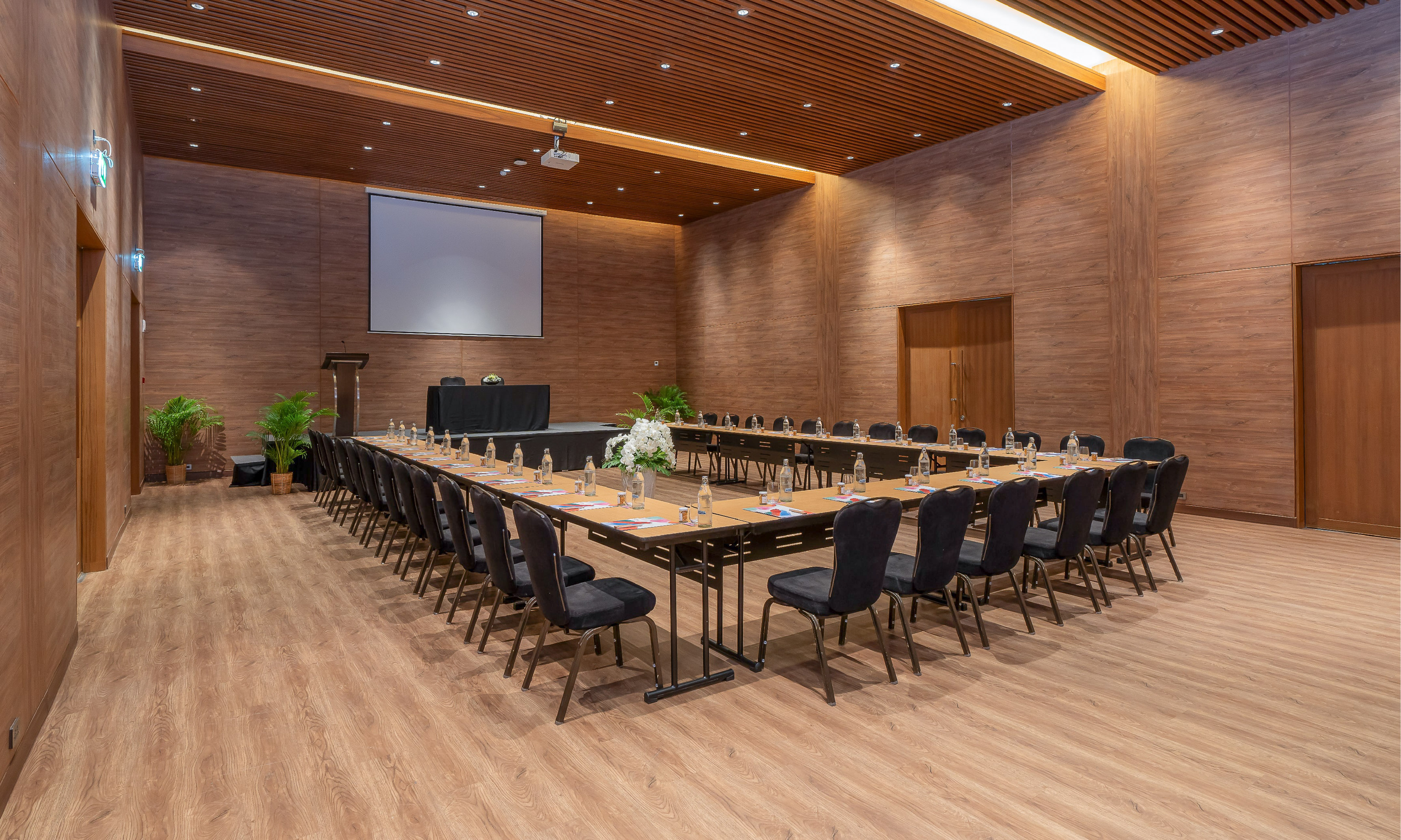Modern U-shape conference room with projector screen and wooden walls.