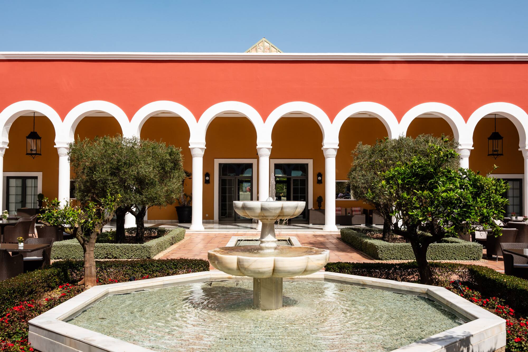 Mediterranean courtyard garden with fountain and red arched building.