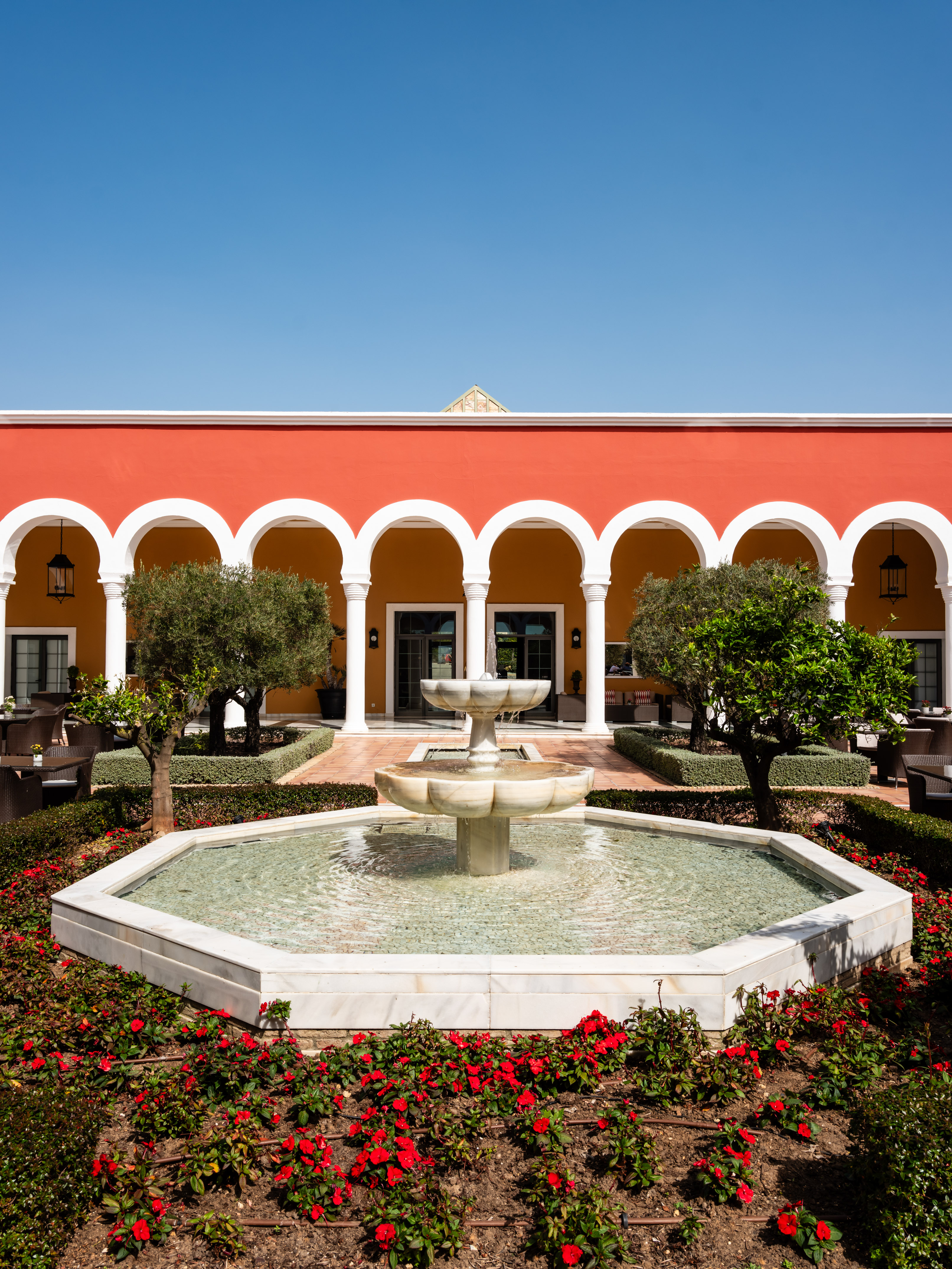 Mediterranean courtyard garden with fountain and red arched building.