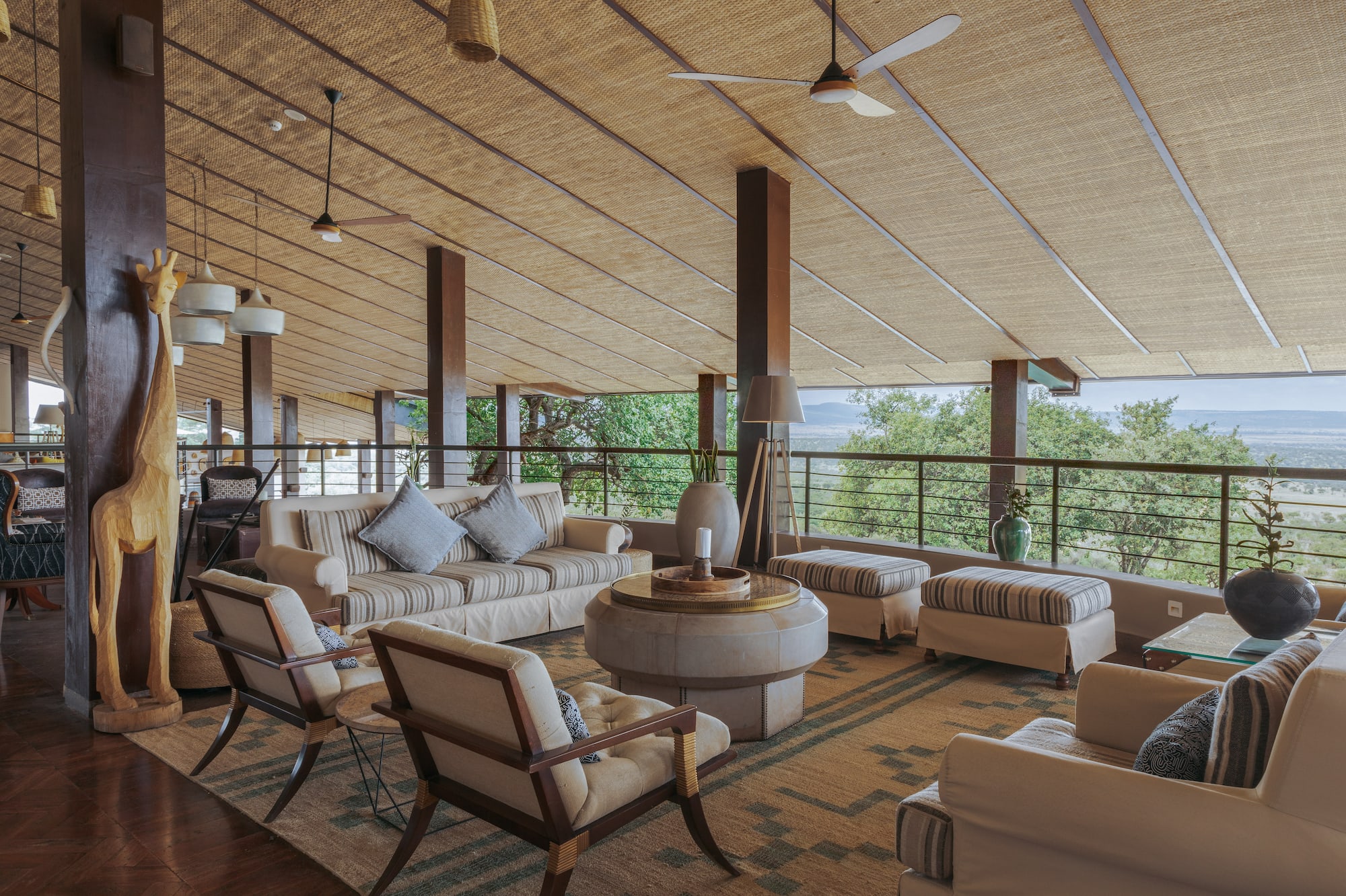 Open-air safari lodge lounge, savanna view, woven ceiling, natural decor.