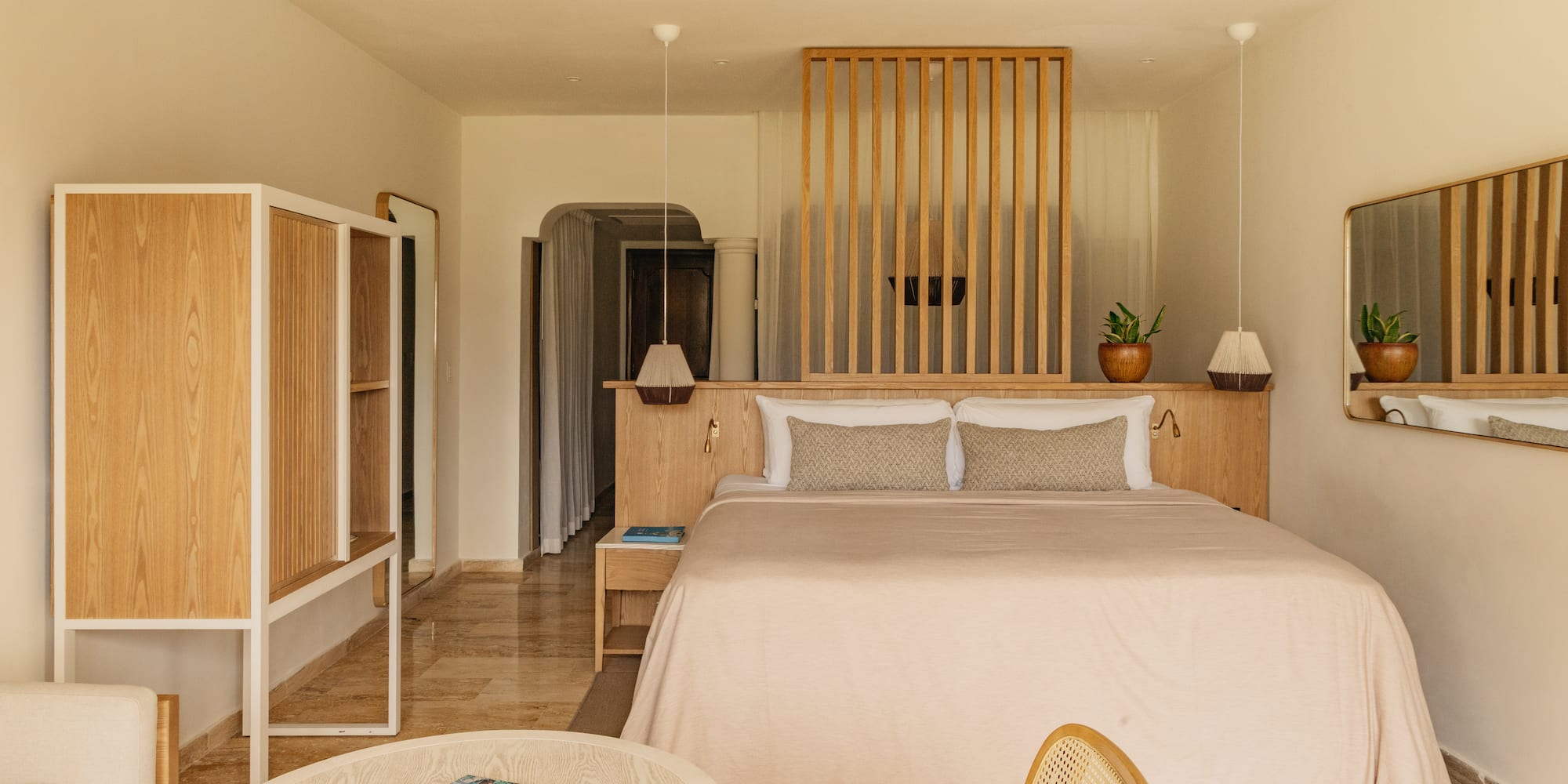 Bright hotel room with wooden slat headboard, king bed, and minimalist decor.