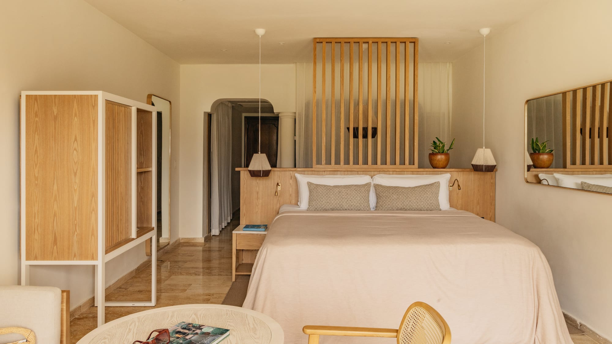 Minimalist hotel bedroom with king bed, wood headboard, and neutral decor.