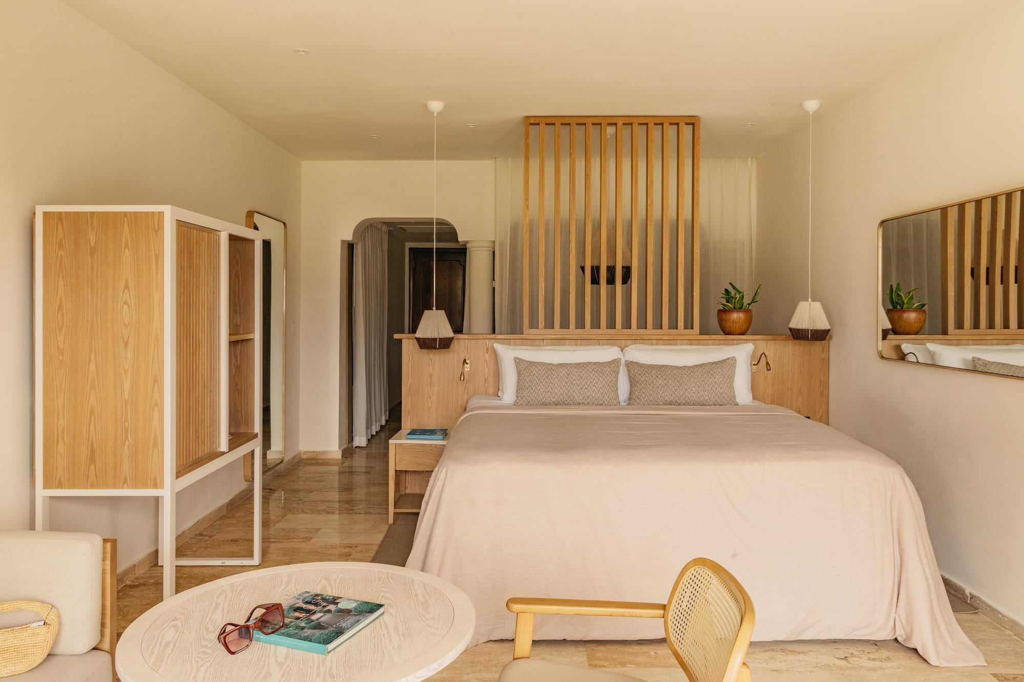 Minimalist hotel bedroom with king bed, wood headboard, and neutral decor.