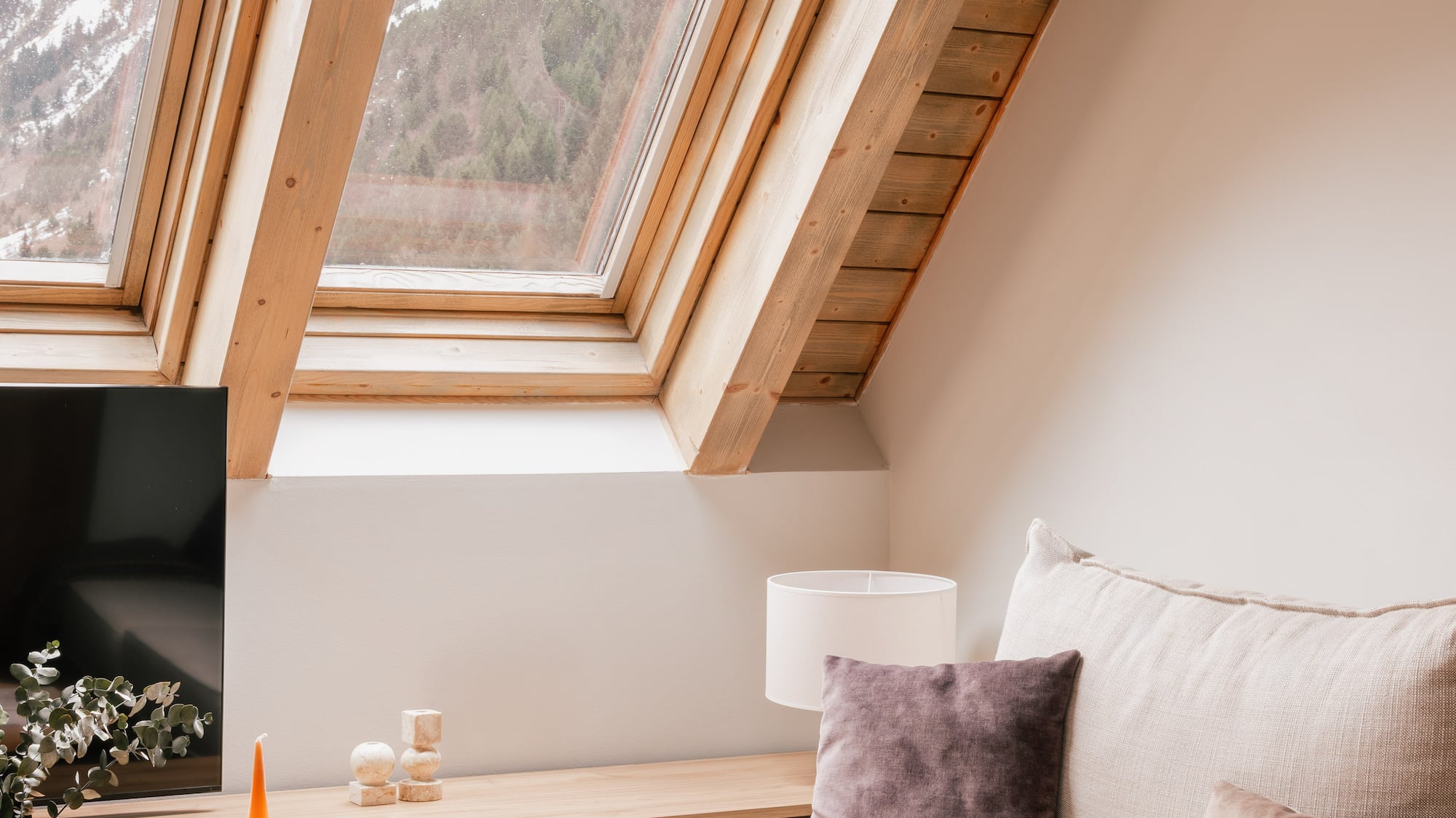 Cozy attic living room with wooden ceiling, mountain view from skylight.
