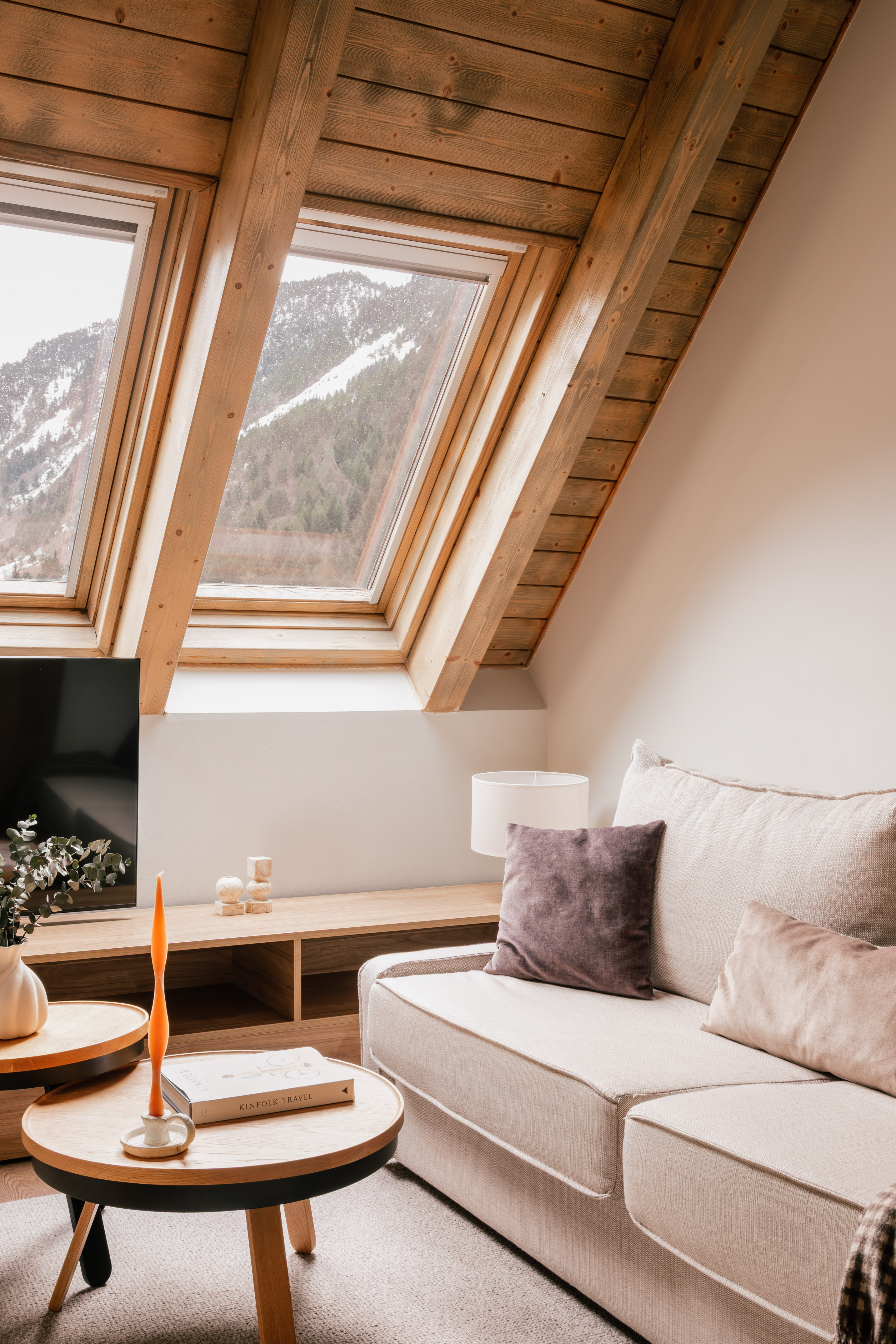 Cozy attic living room with wooden ceiling, mountain view from skylight.