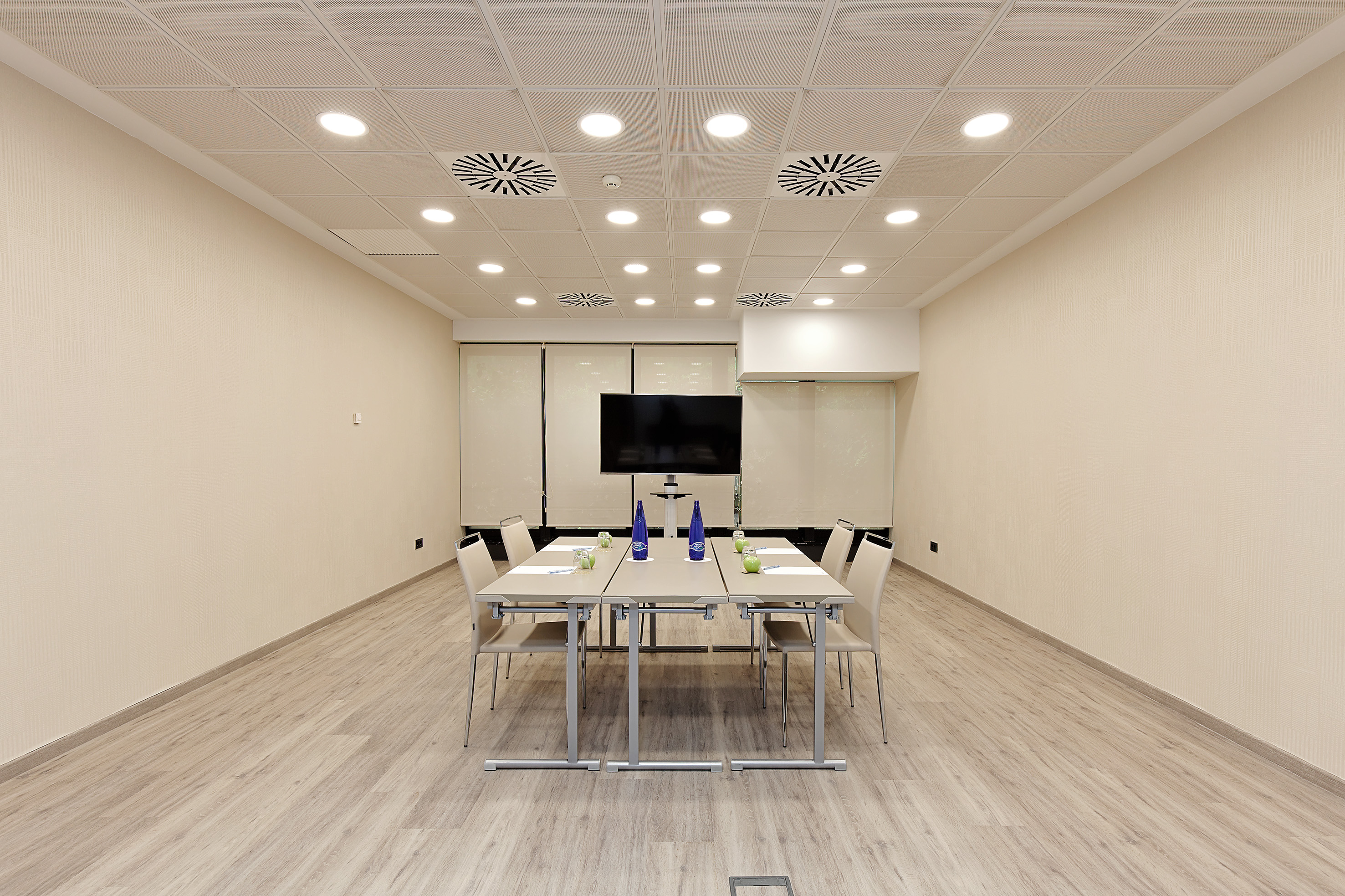 Modern conference room interior with light wood floor, table, chairs, and TV.
