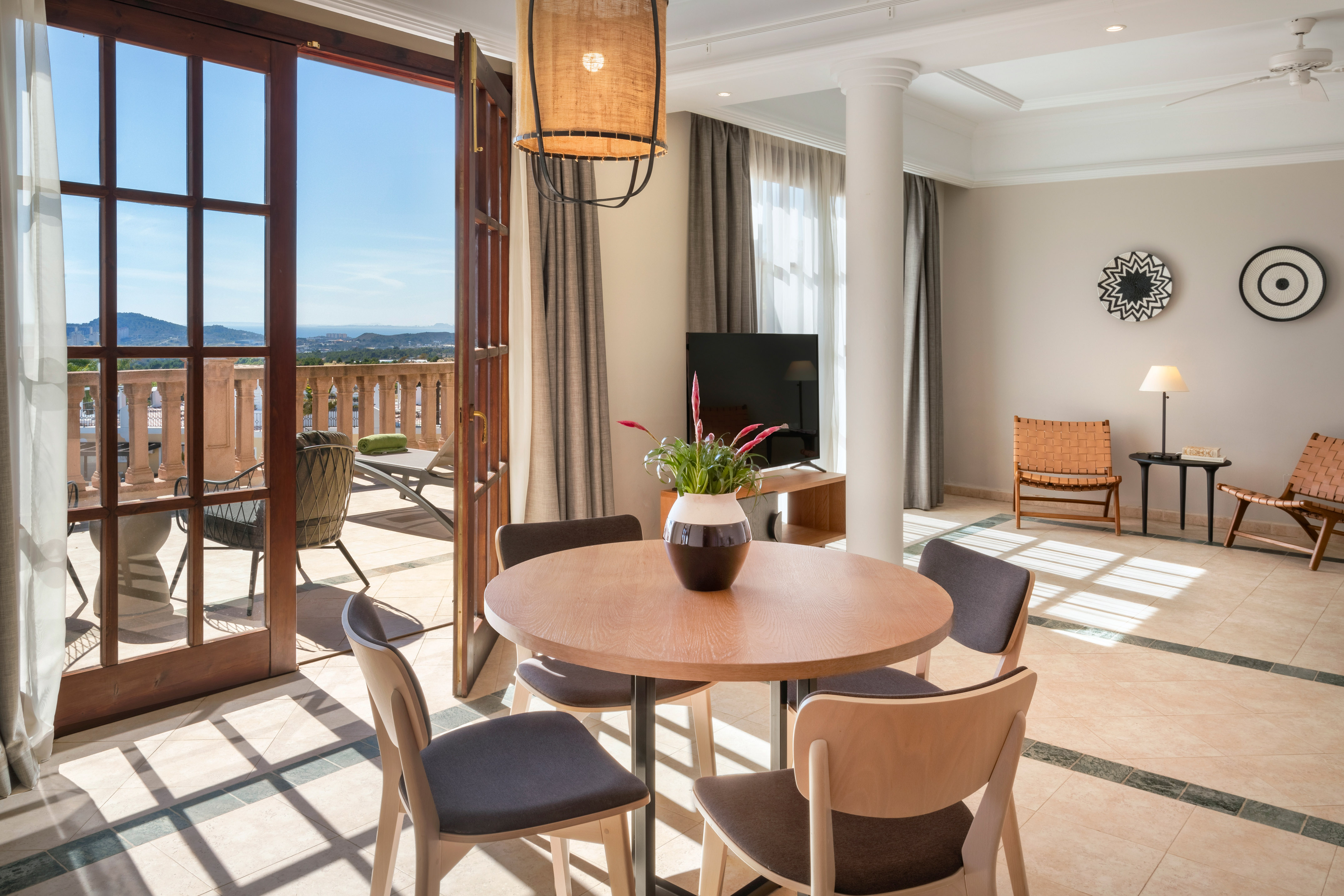 Bright hotel suite with dining area, open balcony, and panoramic sea view.