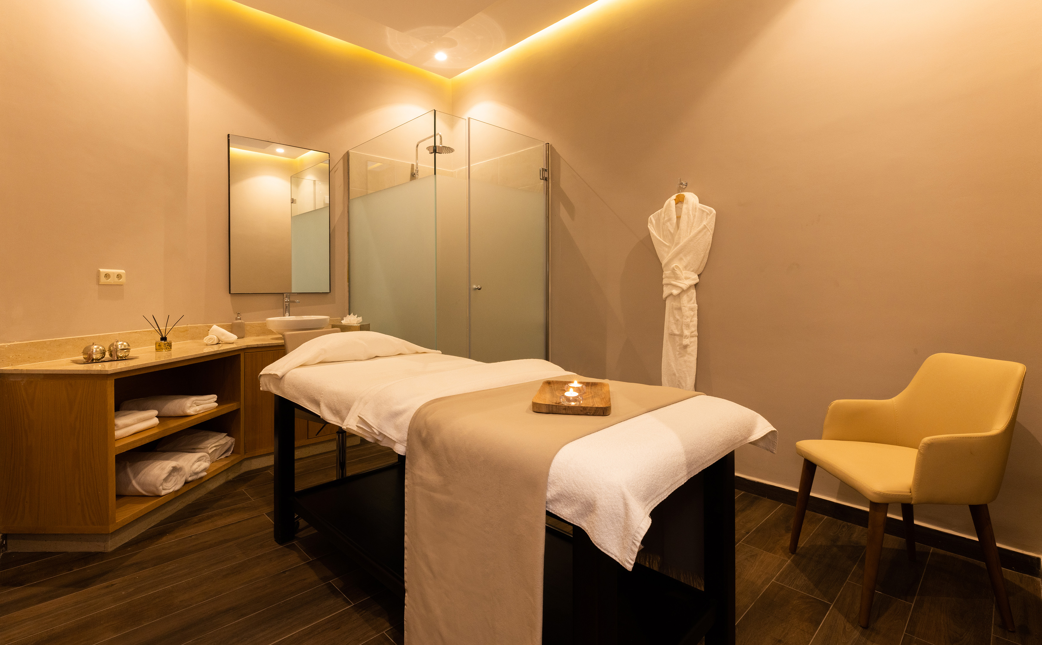 Spa treatment room with massage table, warm lighting, shower, and vanity.