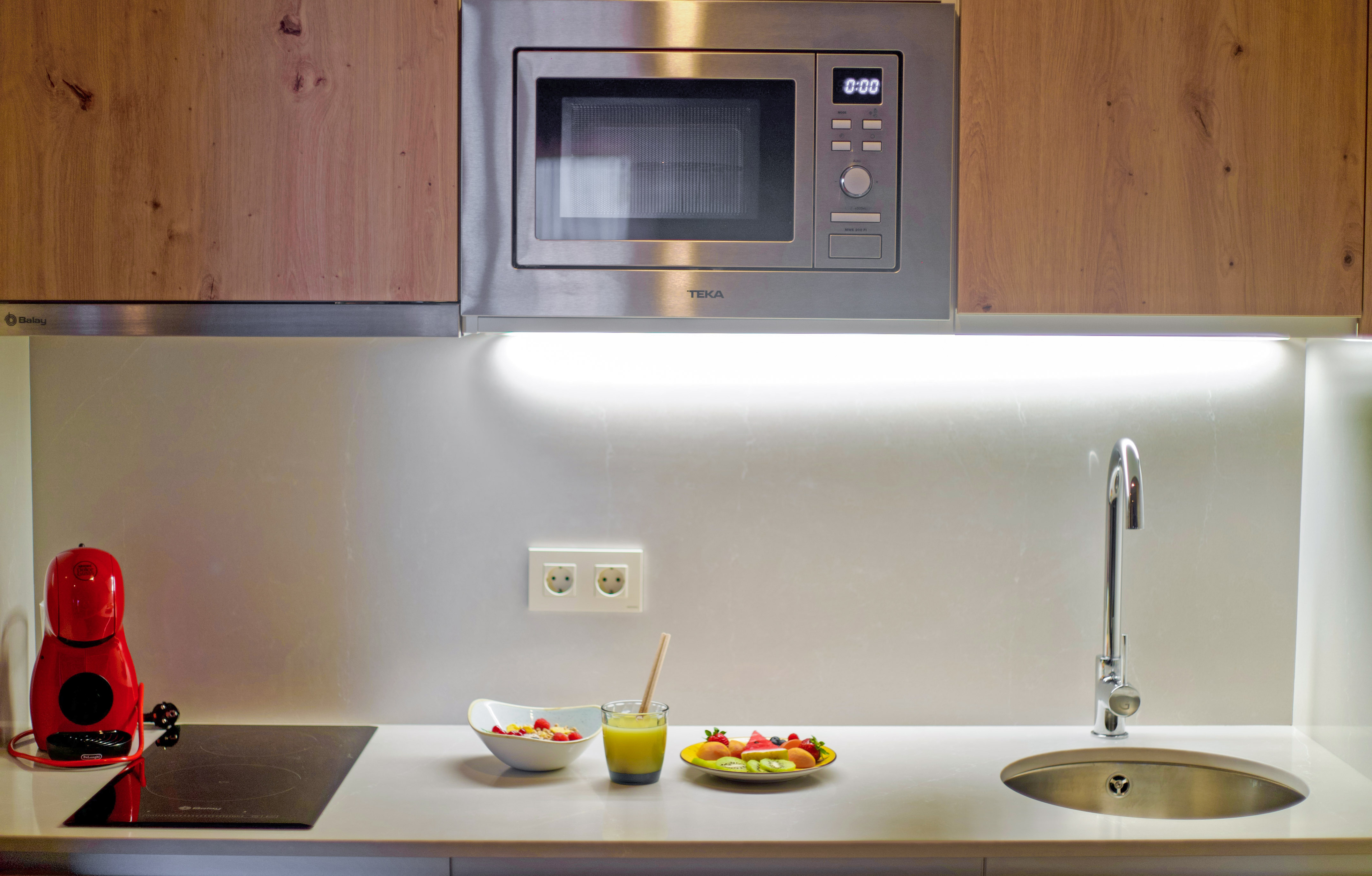a microwave above a sink and a bowl of fruit