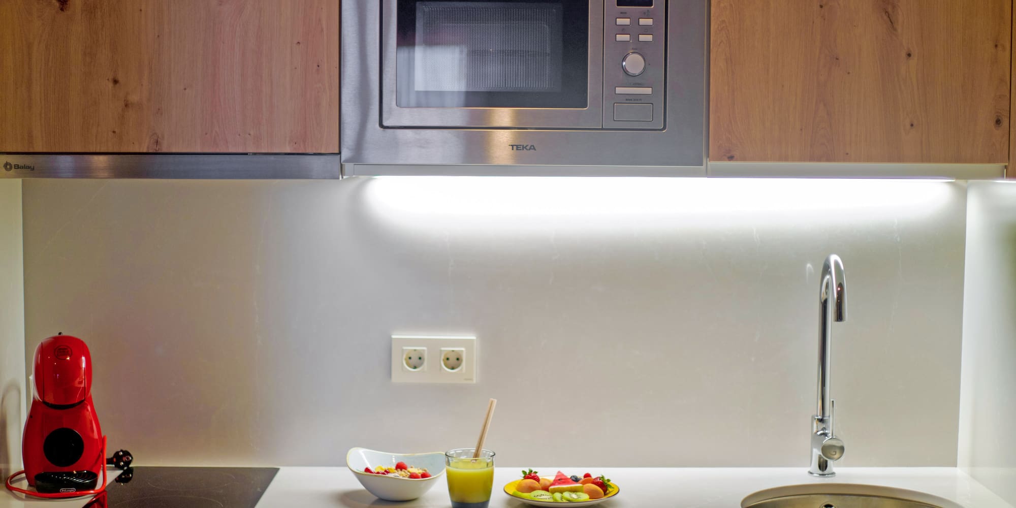 a microwave above a sink and a bowl of fruit