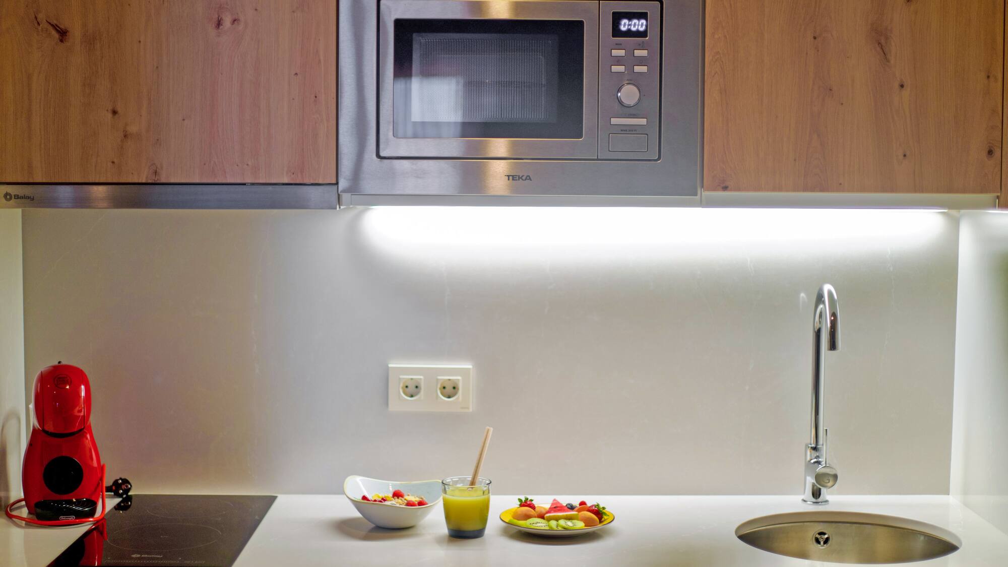 a microwave above a sink and a bowl of fruit