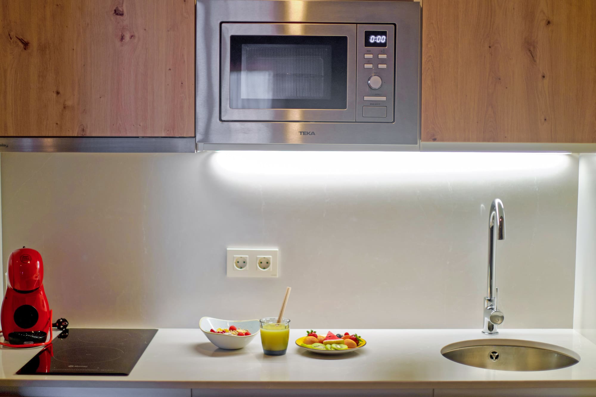 a microwave above a sink and a bowl of fruit