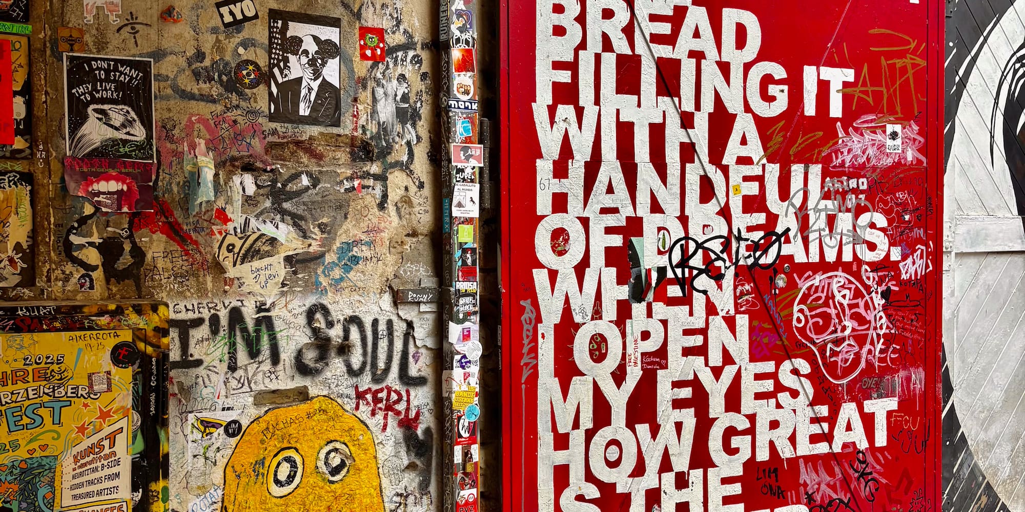 Urban wall with vibrant street art, graffiti, stickers, and a red door featuring white text.