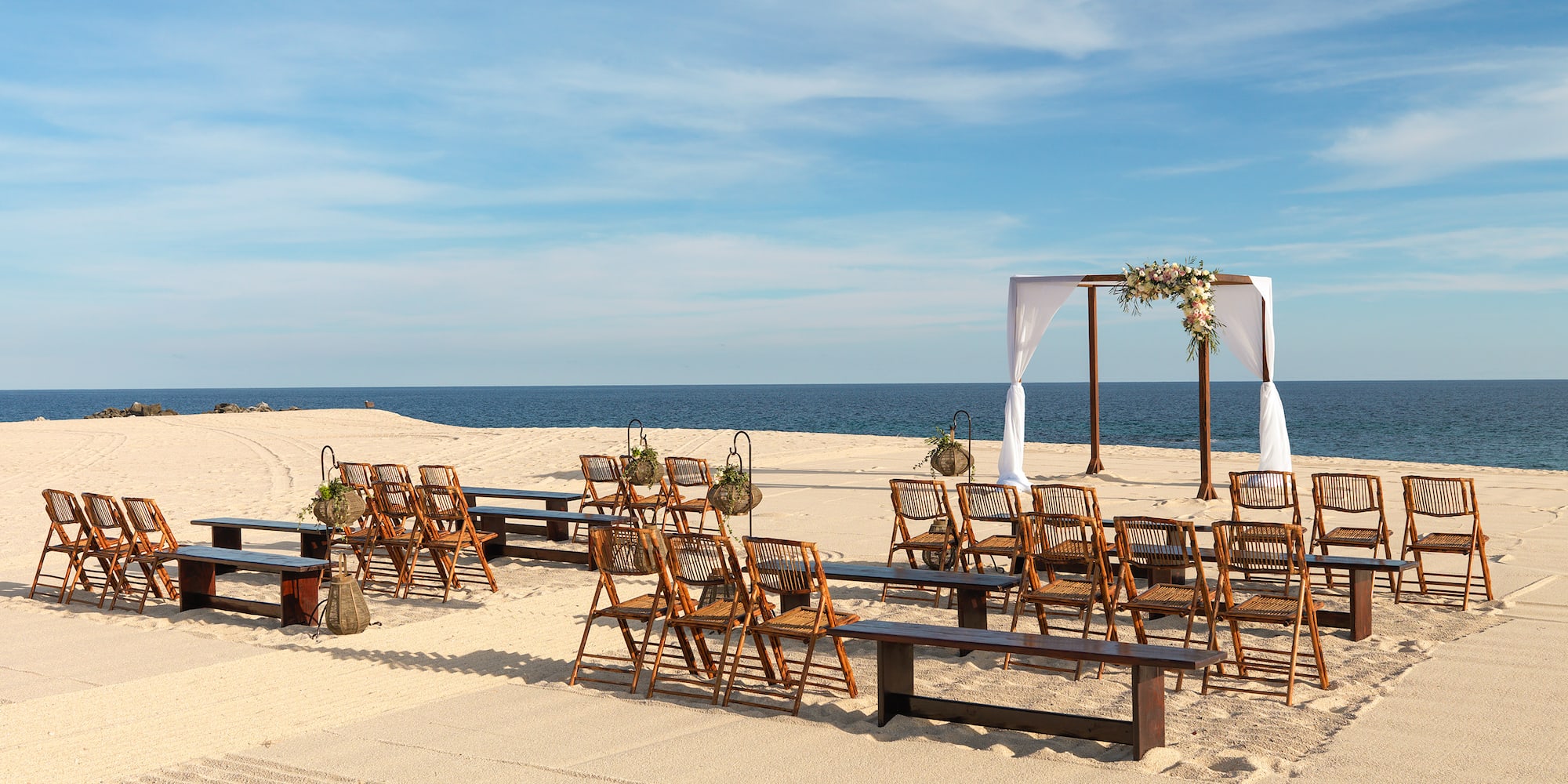 Beach wedding venue with wooden chairs, floral arch, and ocean view. - Playa The Reserve - Paradisus Los Cabos - Adults Only, Los Cabos
