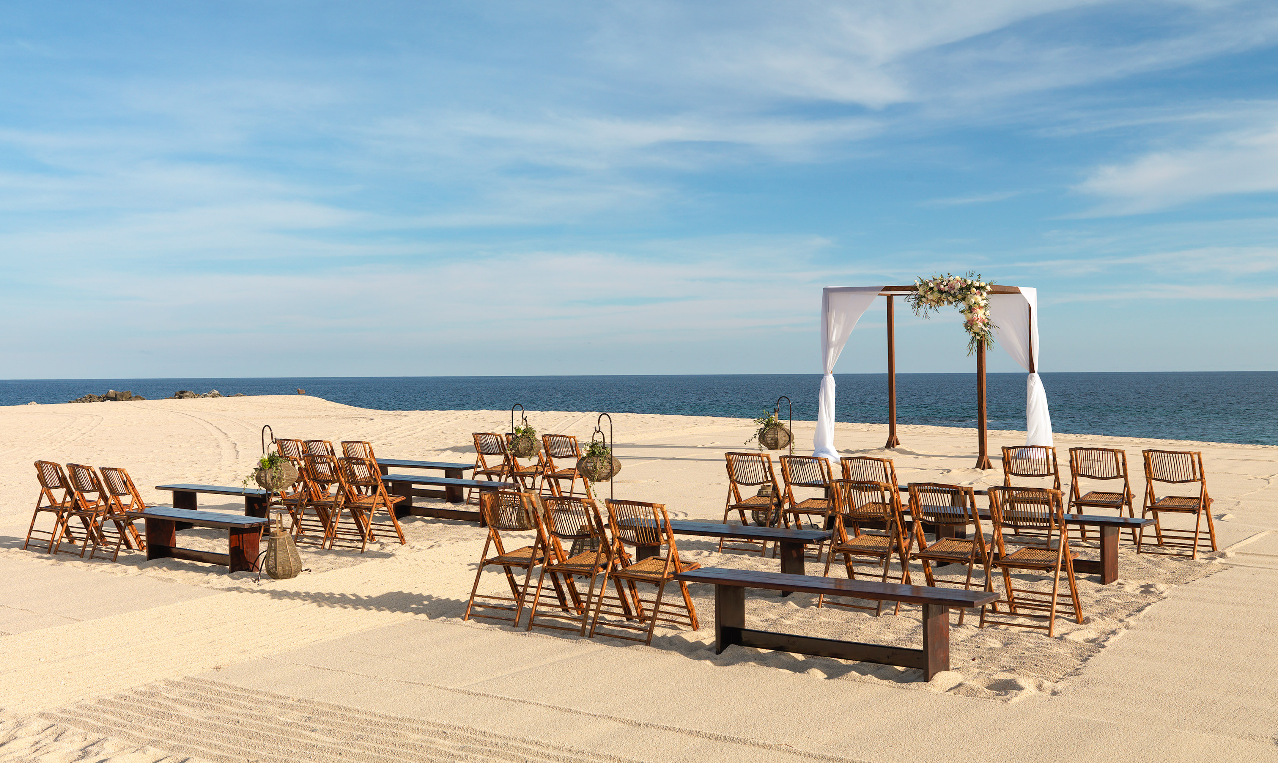 Beach wedding venue with wooden chairs, floral arch, and ocean view. - Playa The Reserve - Paradisus Los Cabos - Adults Only, Los Cabos