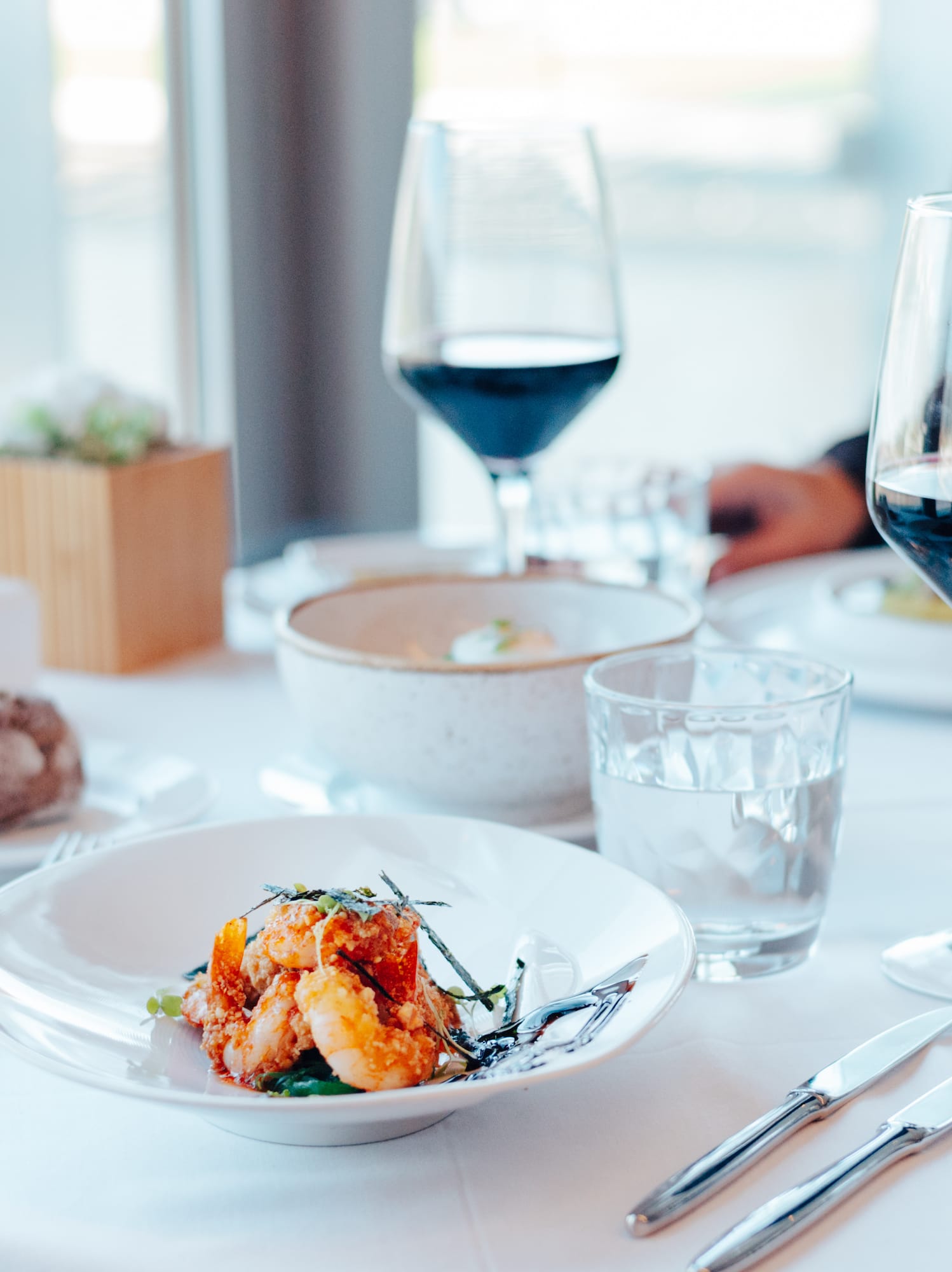 Gourmet shrimp dish, red wine, and bread on an elegant restaurant table.