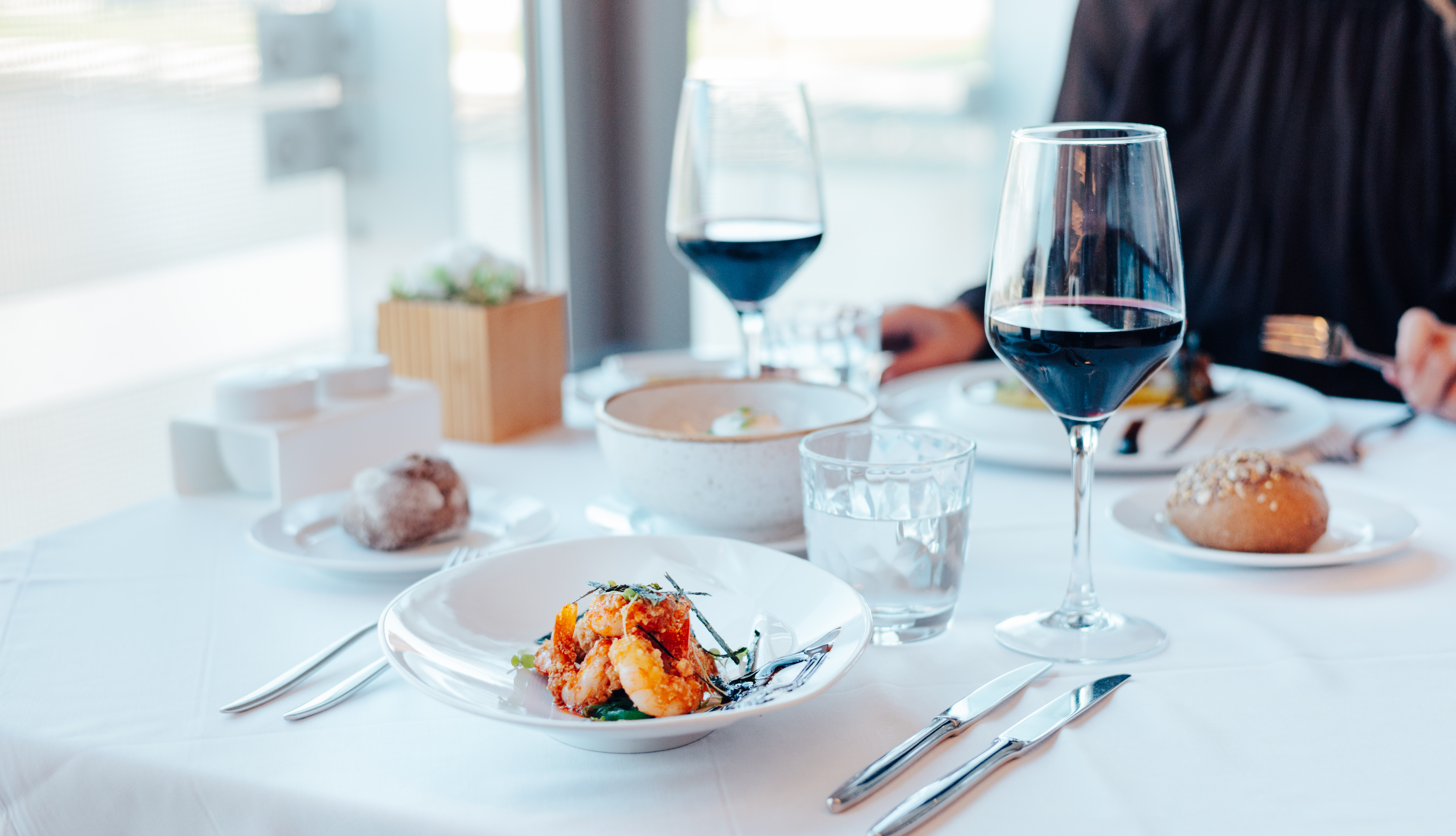Gourmet shrimp dish, red wine, and bread on an elegant restaurant table.