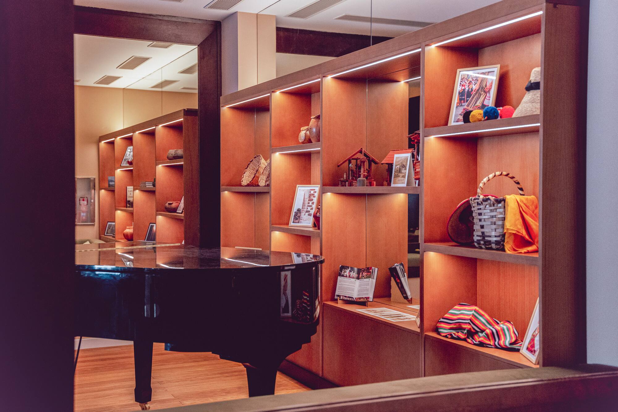 Black grand piano next to illuminated wooden shelves displaying cultural items.