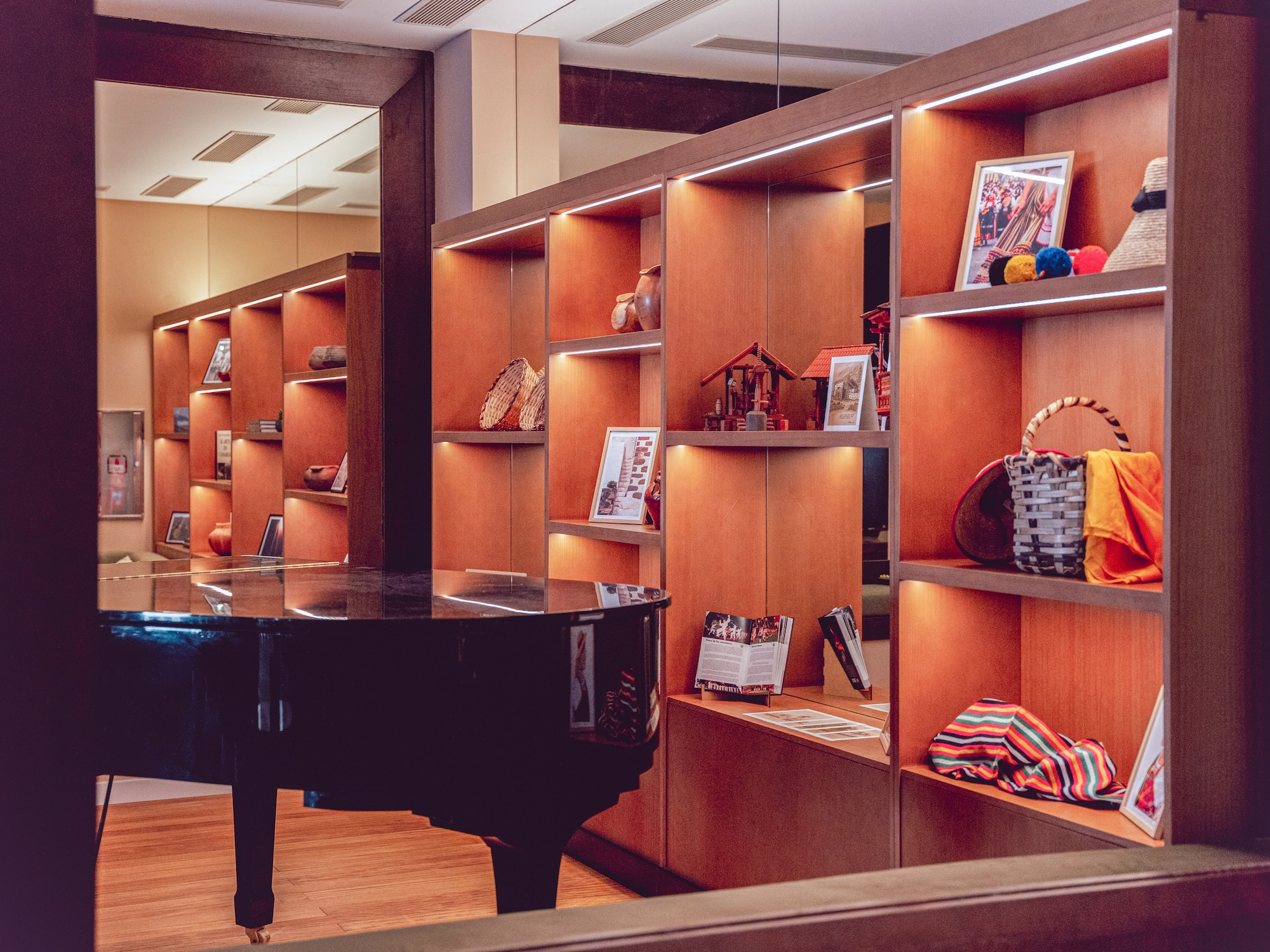 Grand piano and illuminated wooden shelves displaying cultural artifacts.