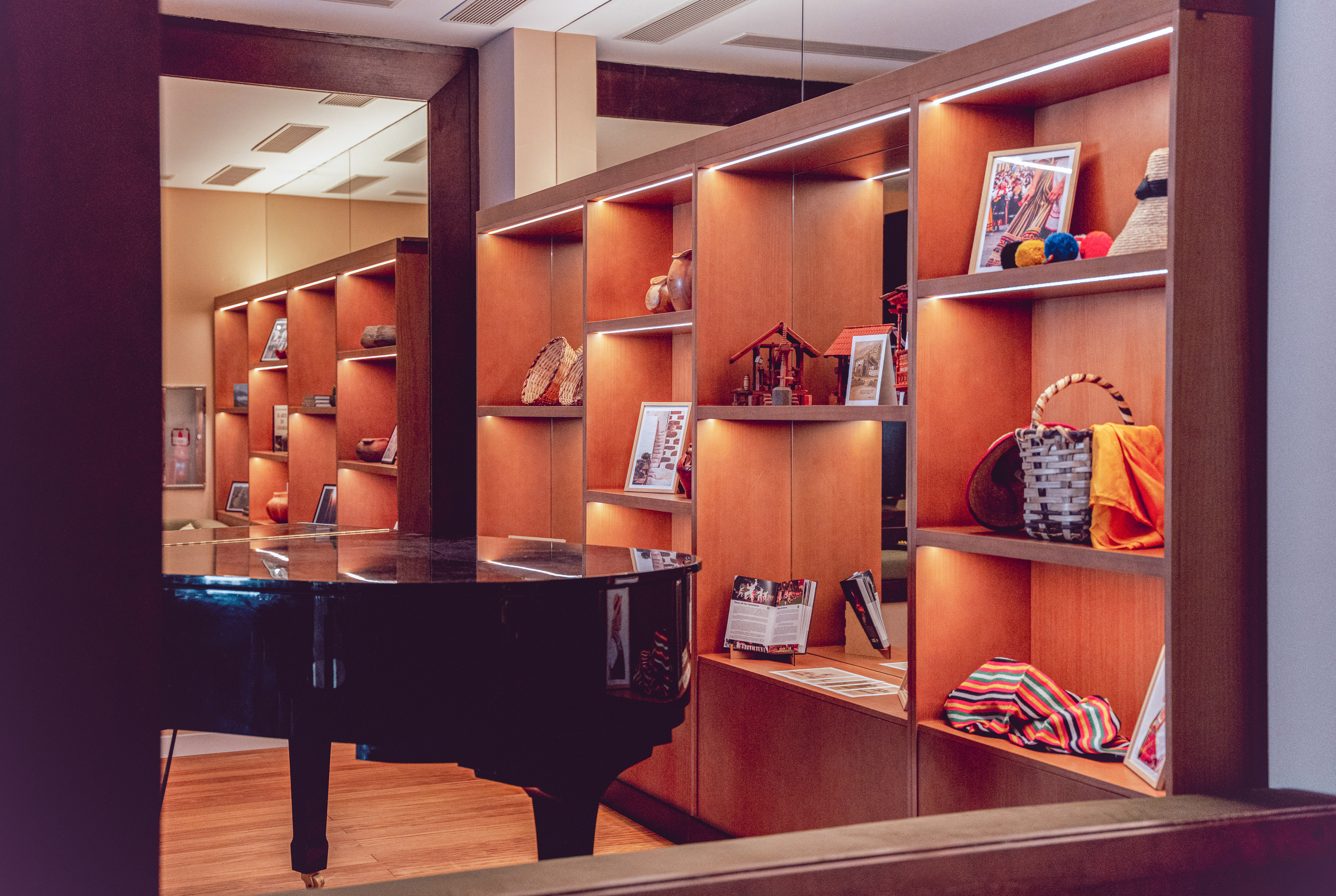 Grand piano and illuminated wooden shelves displaying cultural artifacts.