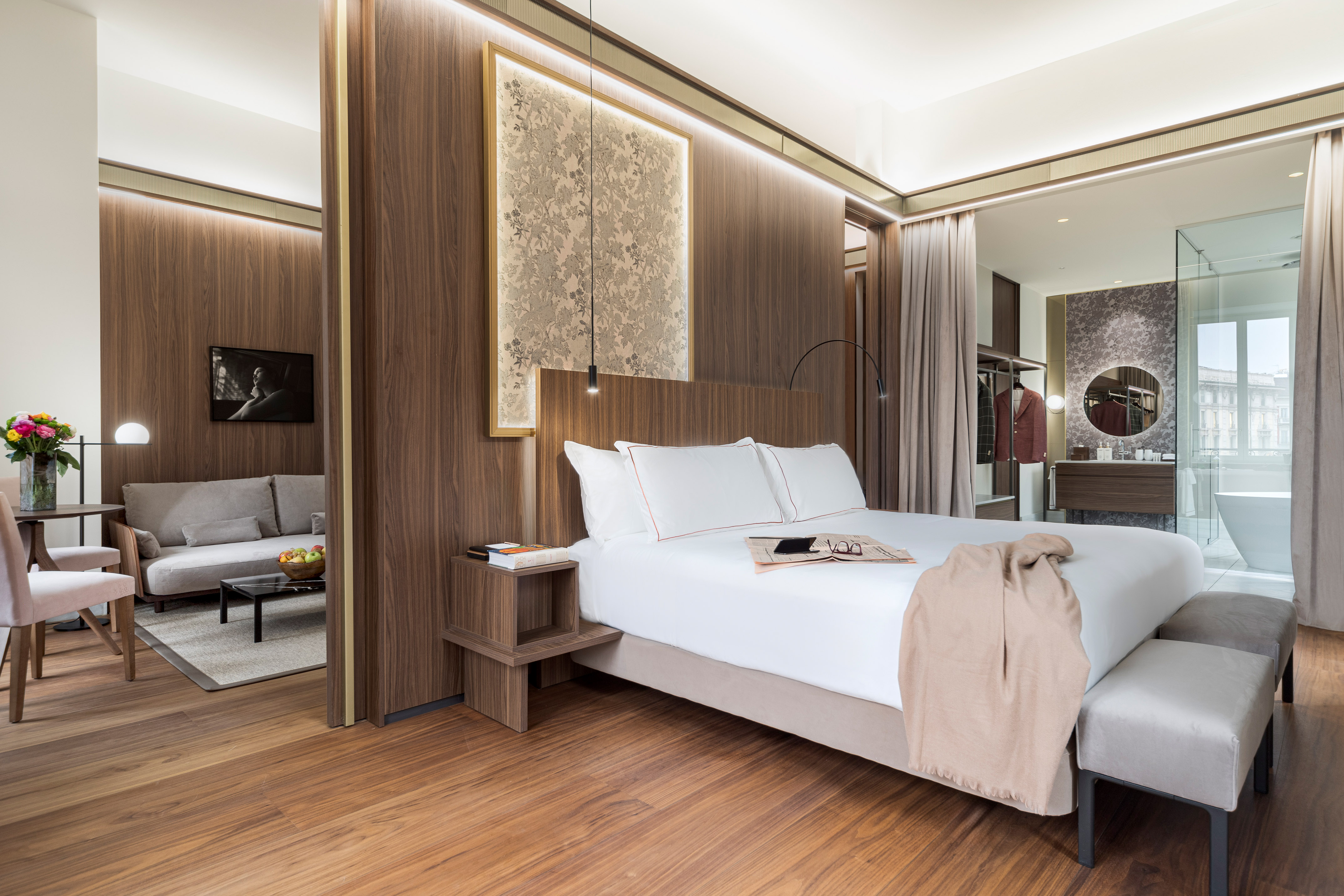 Modern luxury hotel suite with bedroom, living area, and open bathroom.